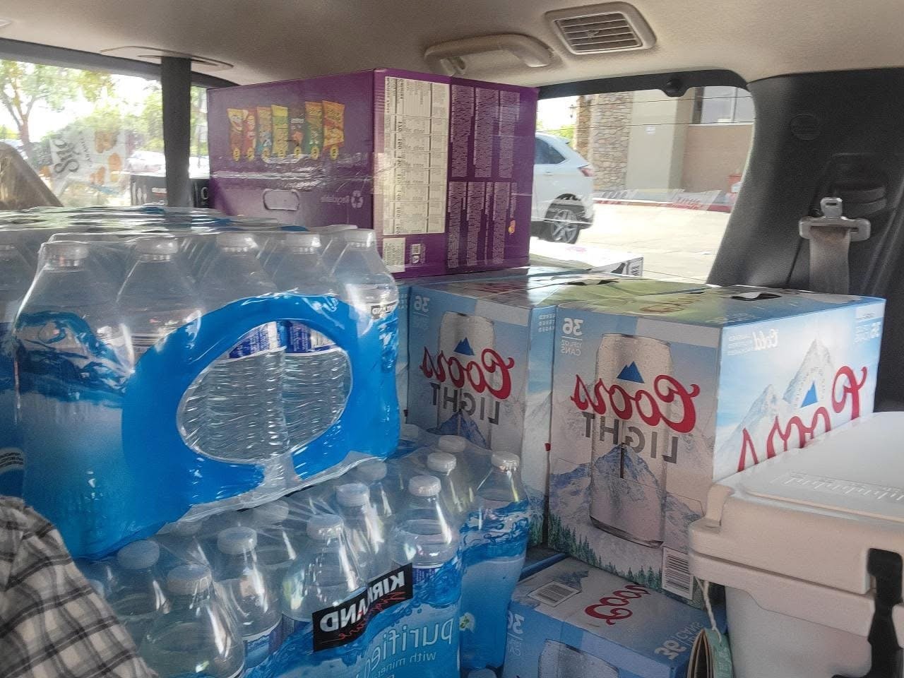 Packaged bottled water, 36-pack, and a case of Light Beer in the back seat of a vehicle.