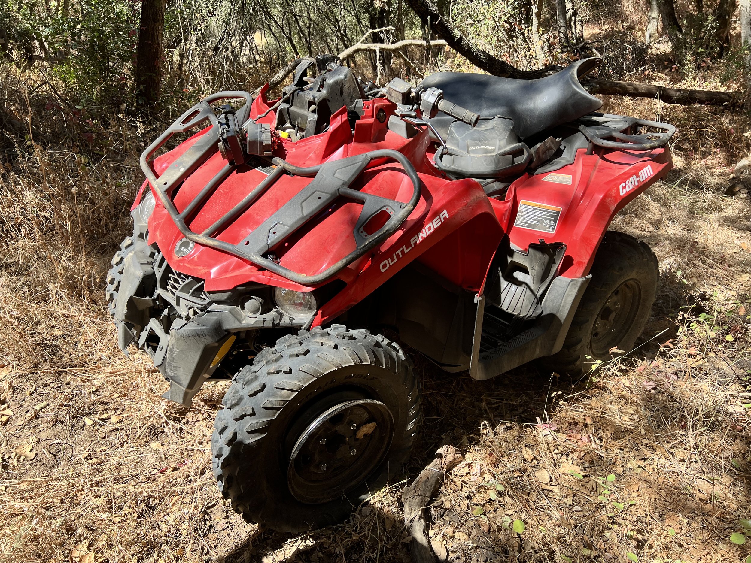 A red Can-Am Outlander all-terrain vehicle on a dirt trail in a wooded area.