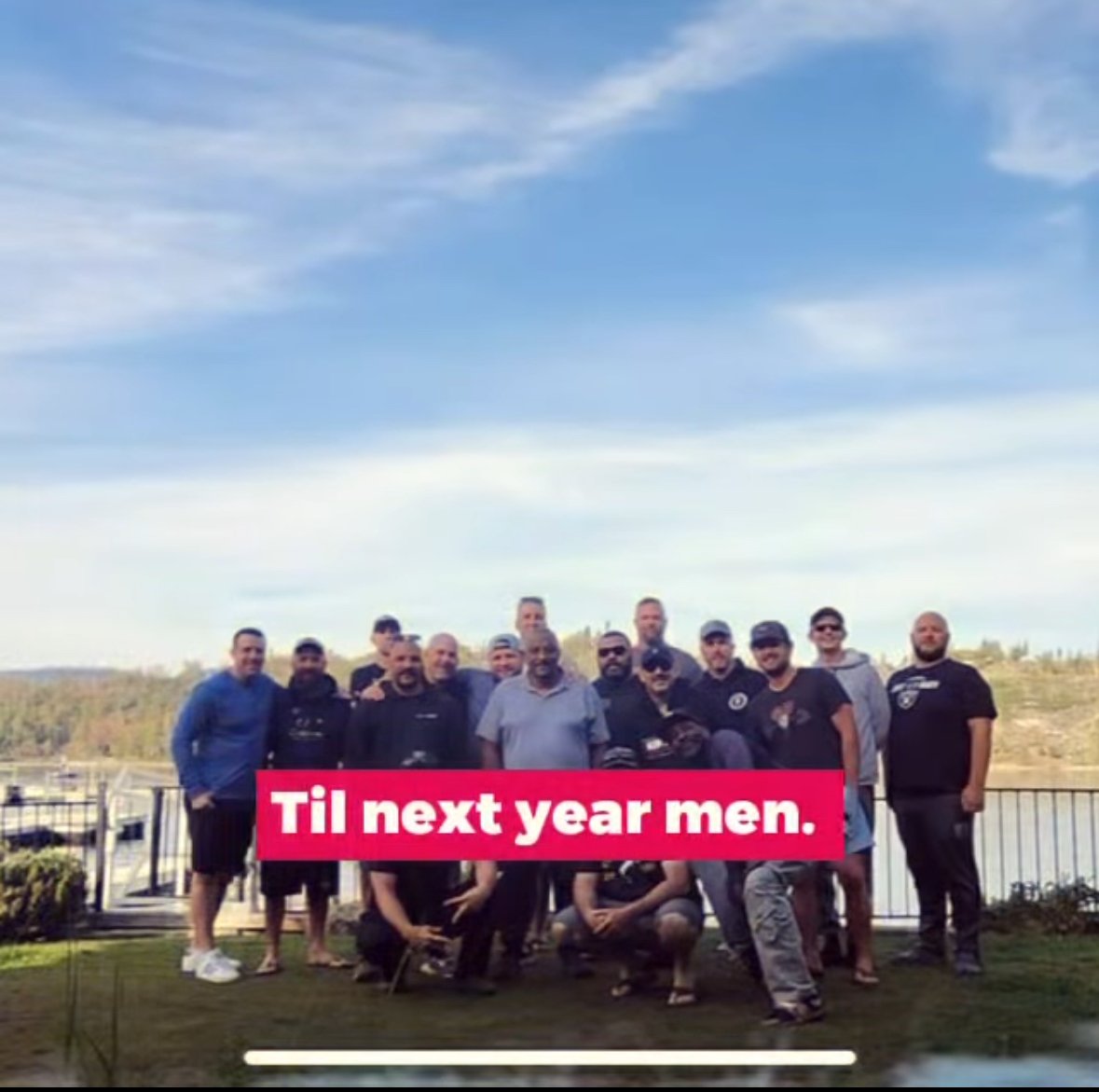 Group of men standing outdoors on a grassy area with a fence and a scenic view of hills in the background. Text overlay reads 'Til next year men.'