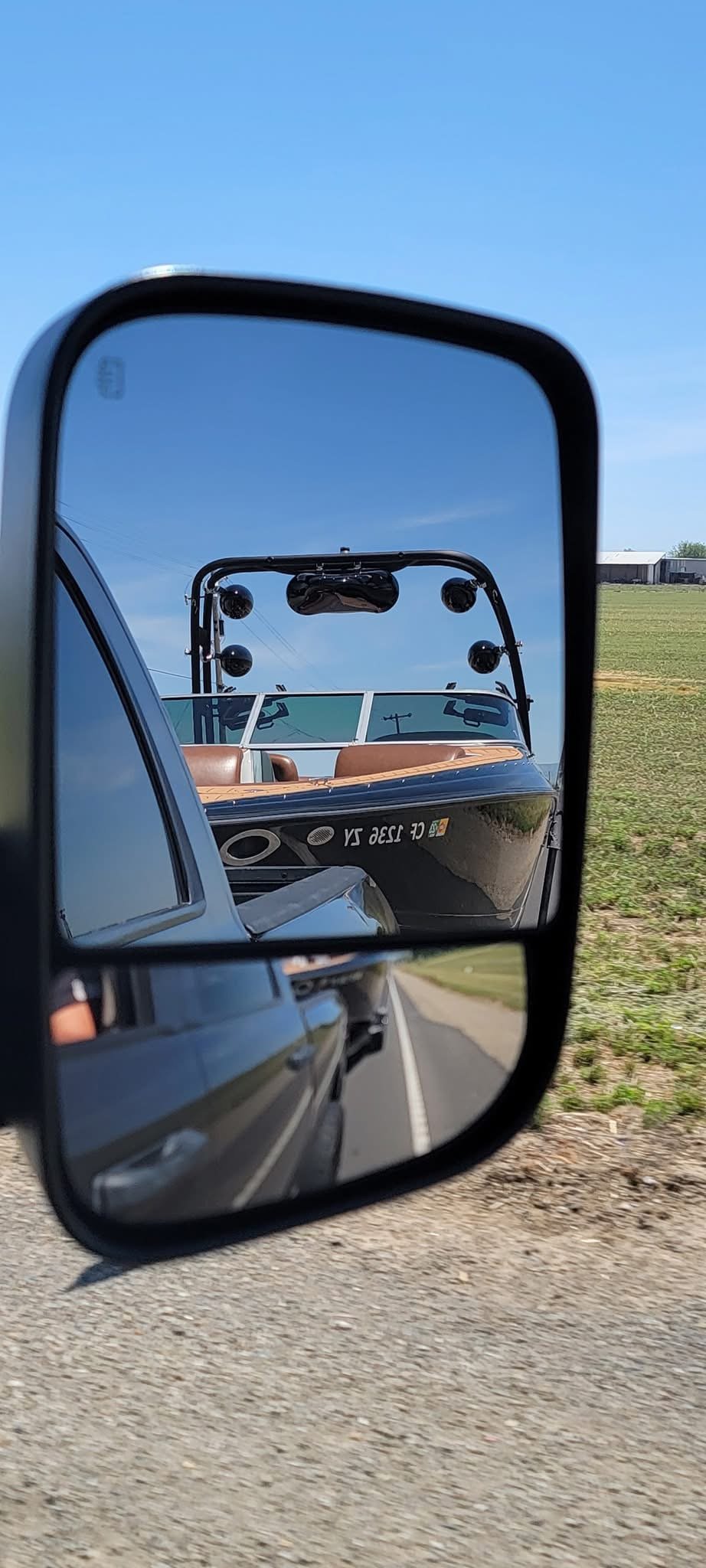 A boat seen in the reflection of a vehicle's side mirror on a rural road.