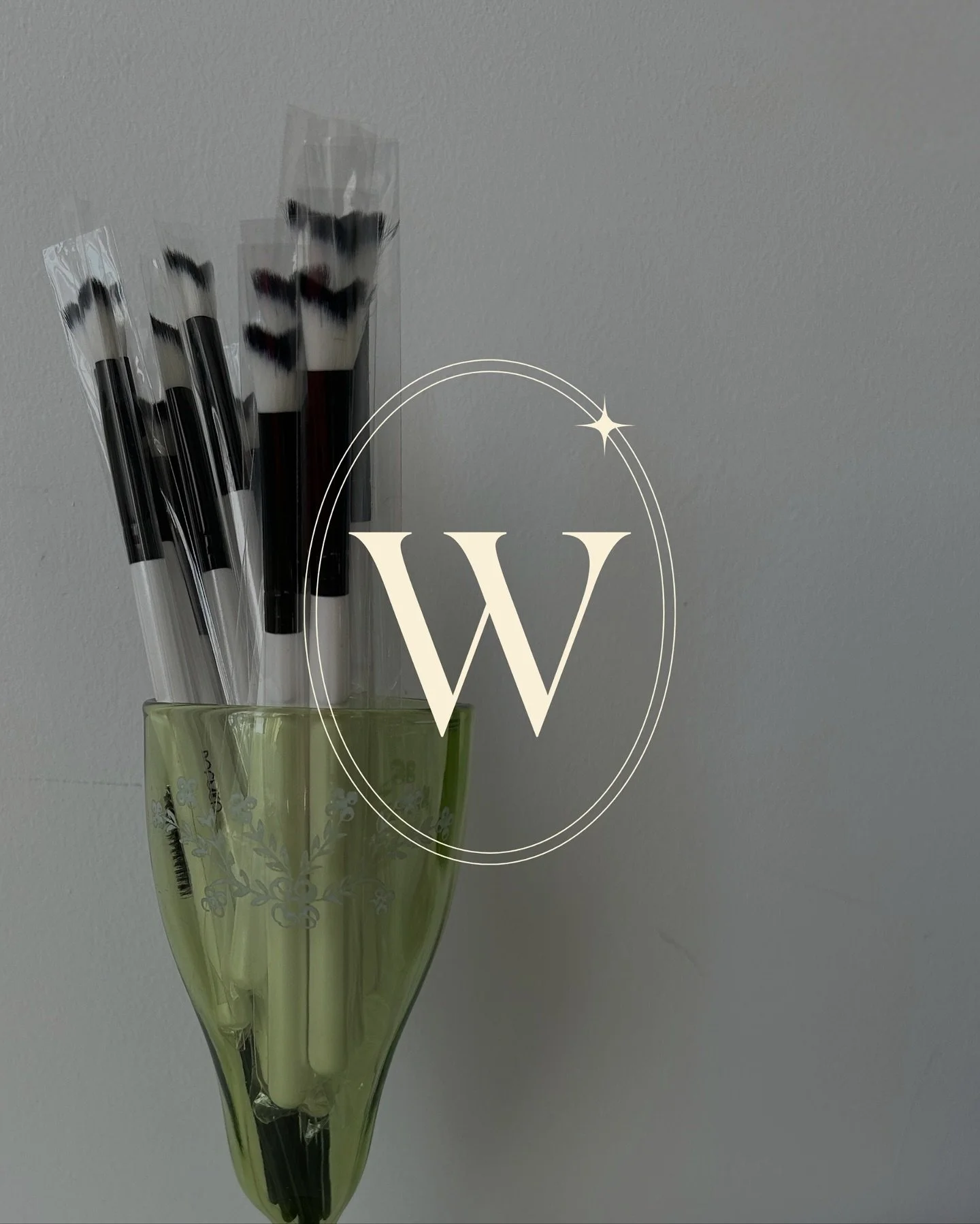 A green vase with white floral patterns holding five black and white paintbrushes with black tips and plastic wrapping.