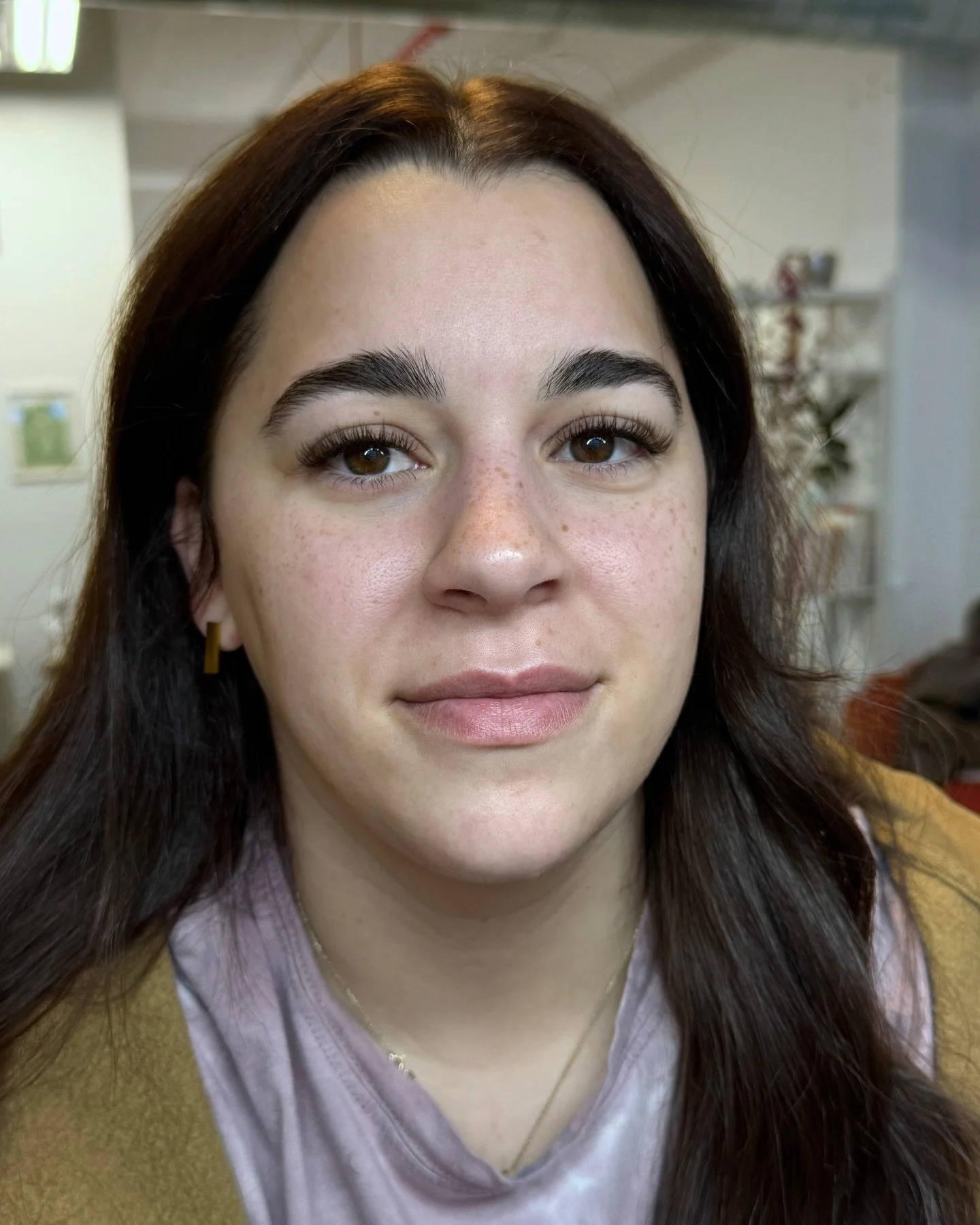 Close-up of a young woman with brown hair, brown eyes, light skin with freckles, and wearing a yellow top.