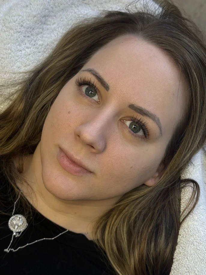 Close-up of a young woman with light skin, brown hair, and blue-green eyes lying on a soft surface.