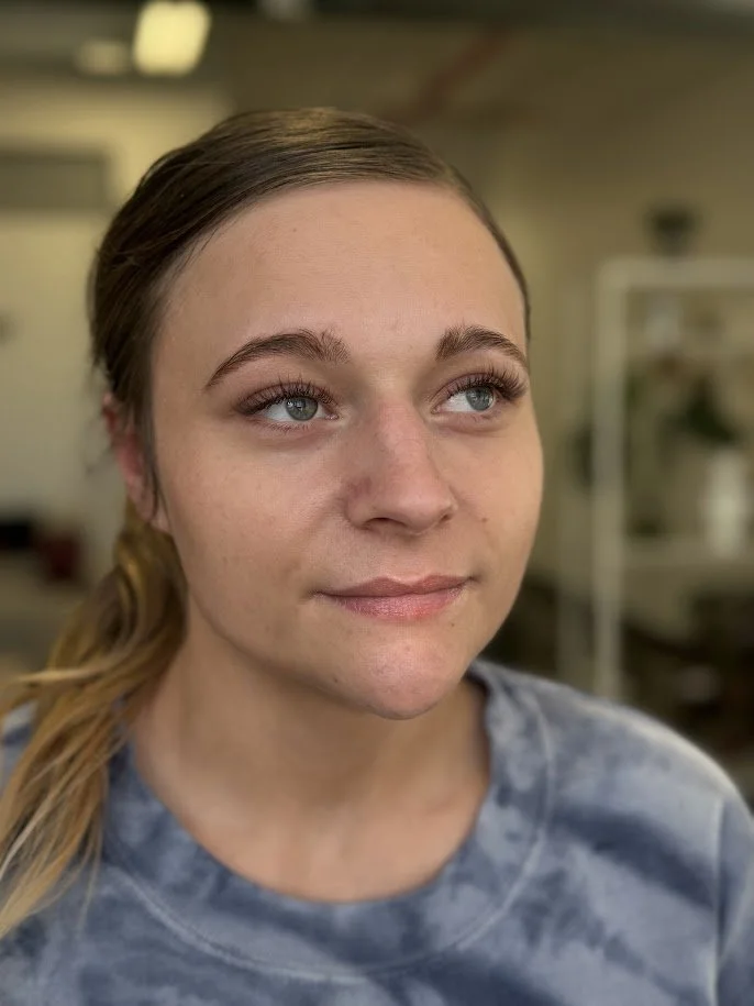 A young woman with light skin, light blue eyes, and light brown hair tied back, looking slightly to her right with a neutral expression.