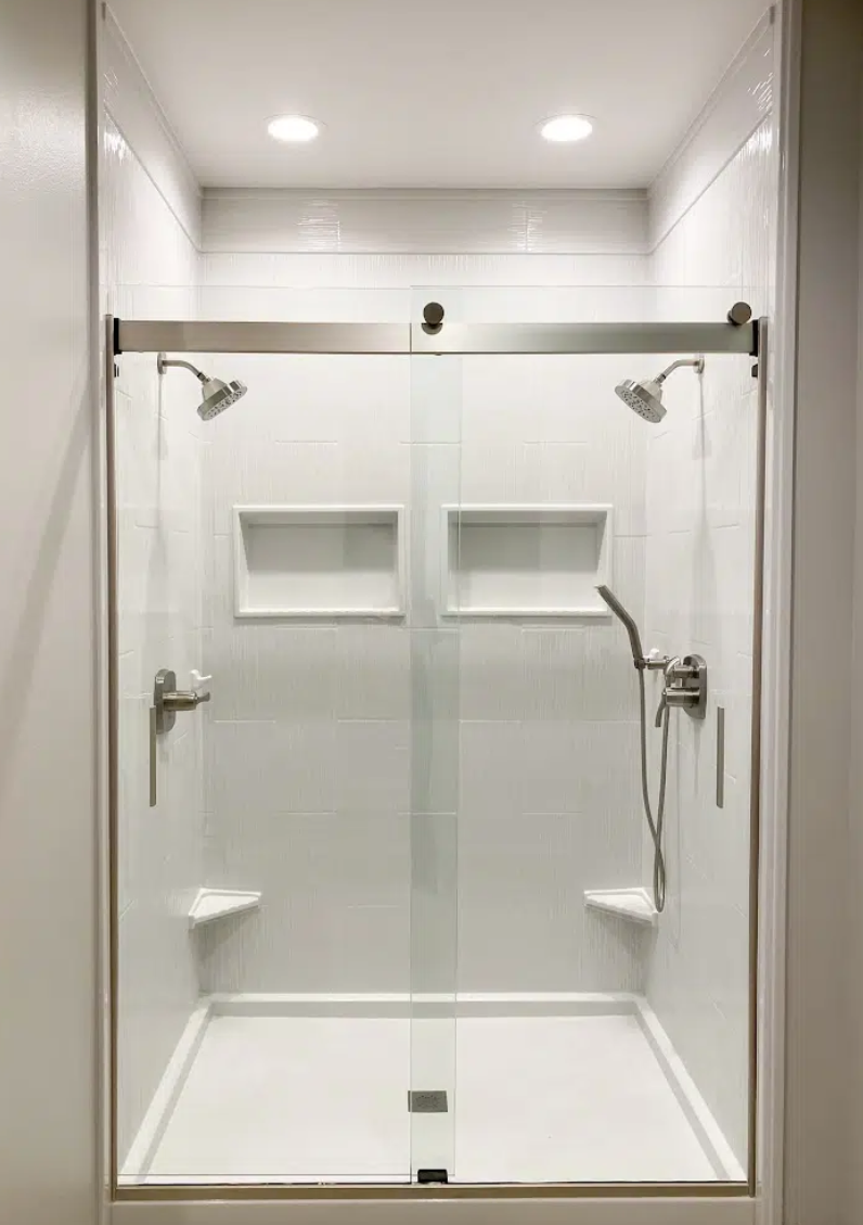 Empty walk-in shower with glass door, dual showerheads, built-in shelves, and a hand-held shower wand.