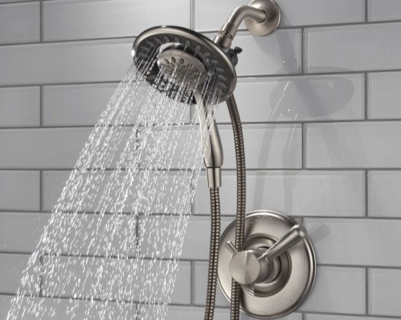 Showerhead spraying water in a bathroom with gray tiled wall.