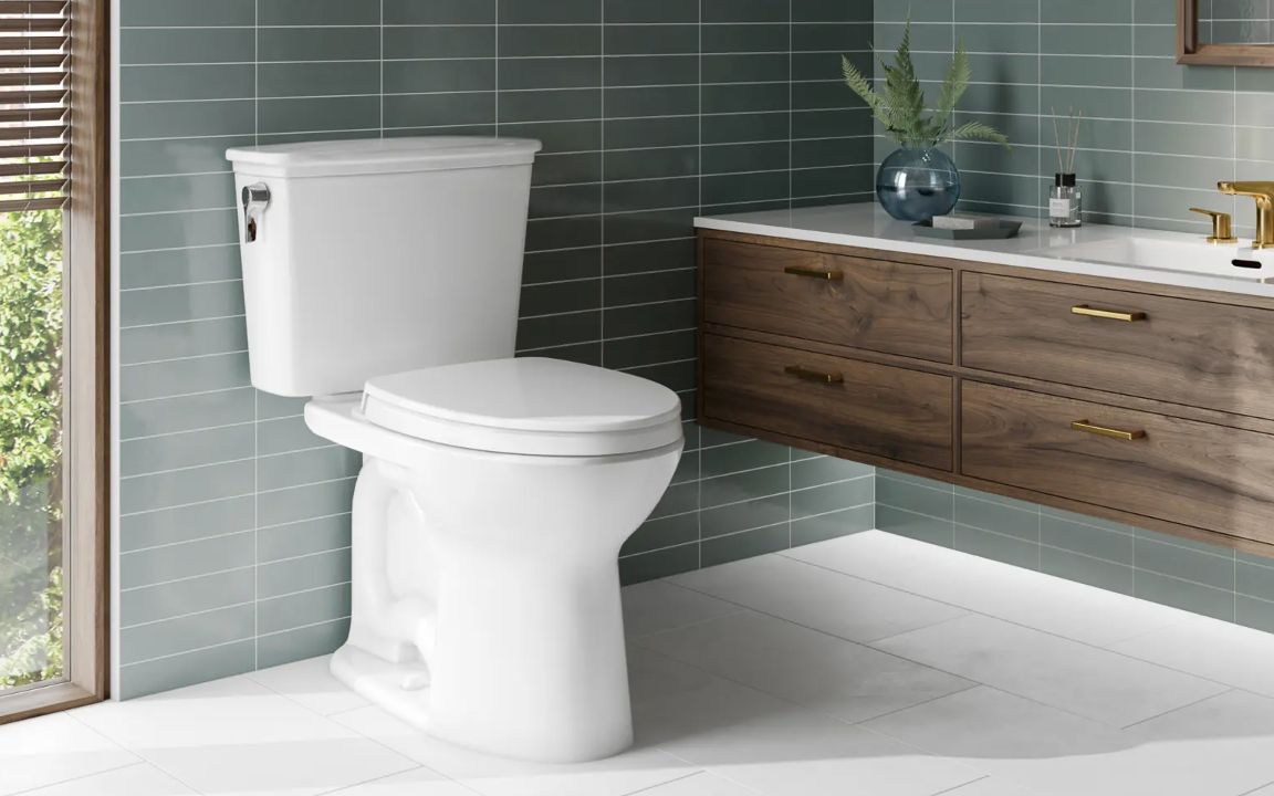Modern bathroom with a white toilet, green tiled walls, and a wooden vanity with a white countertop and gold fixtures.