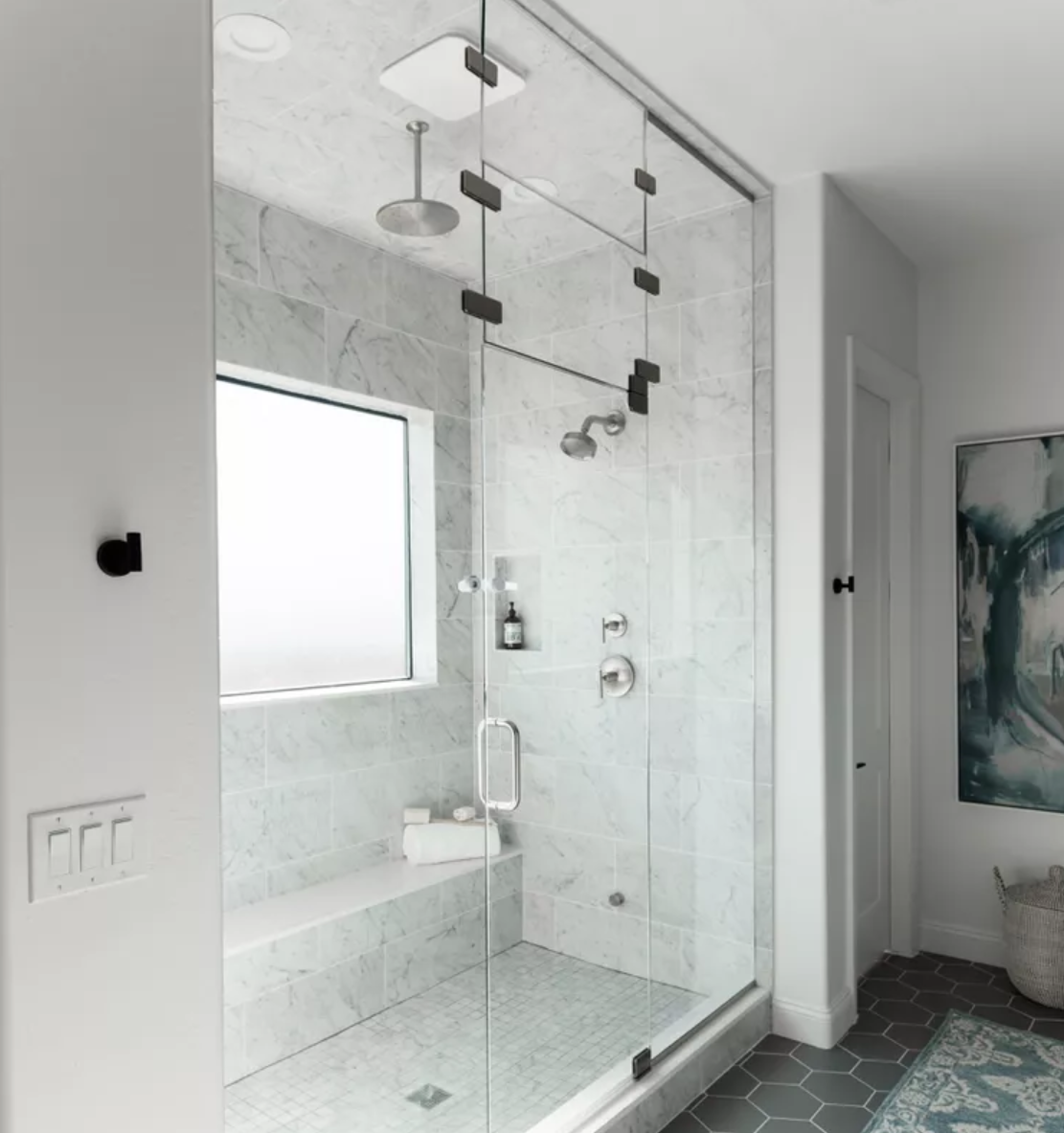 Modern walk-in shower with glass enclosure, marble walls, and black fixtures in a bathroom with dark hexagonal tile flooring and a window providing natural light.
