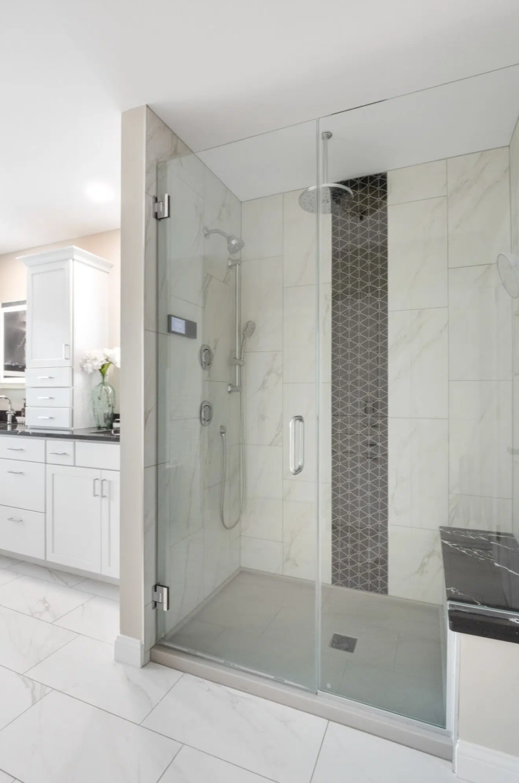 Modern glass-enclosed shower with marble tiles, a black patterned accent strip, and a rain showerhead in a bright white bathroom.