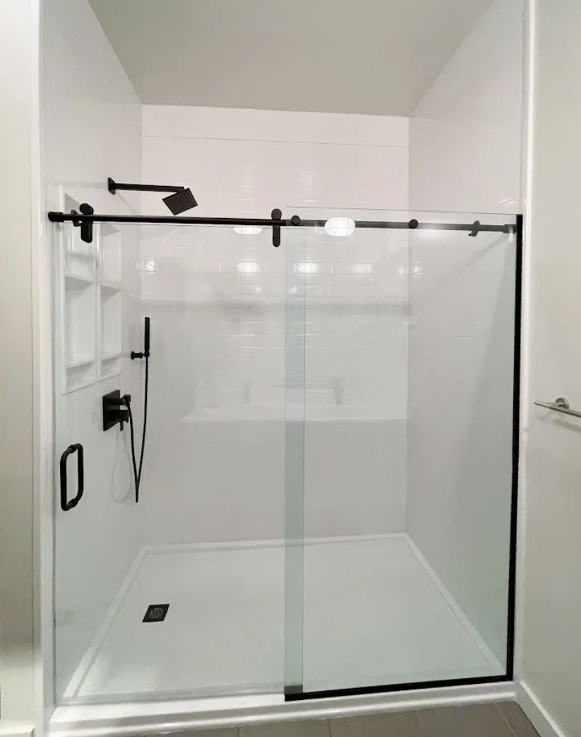 A modern walk-in shower with clear glass sliding doors, black fixtures, a showerhead, hand-held shower, built-in niche, and a tiled floor with a drain.