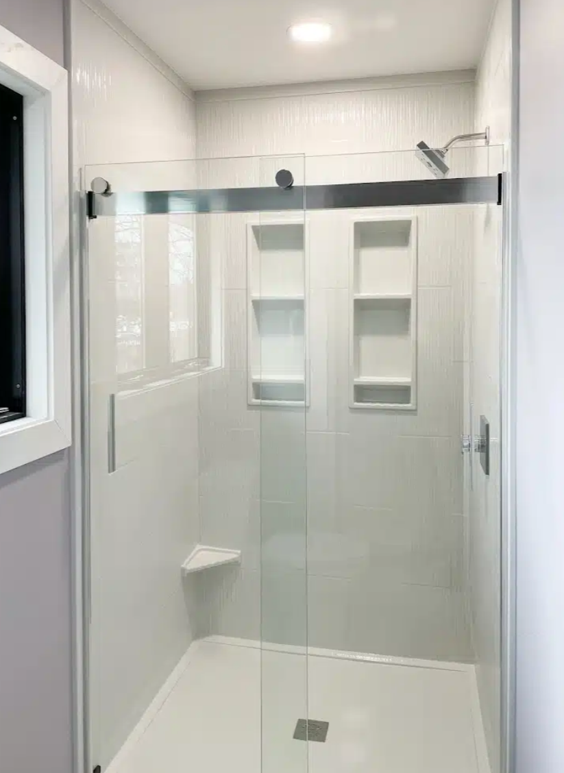Modern walk-in shower with glass door, built-in shelves, and a rain showerhead in a bright bathroom.