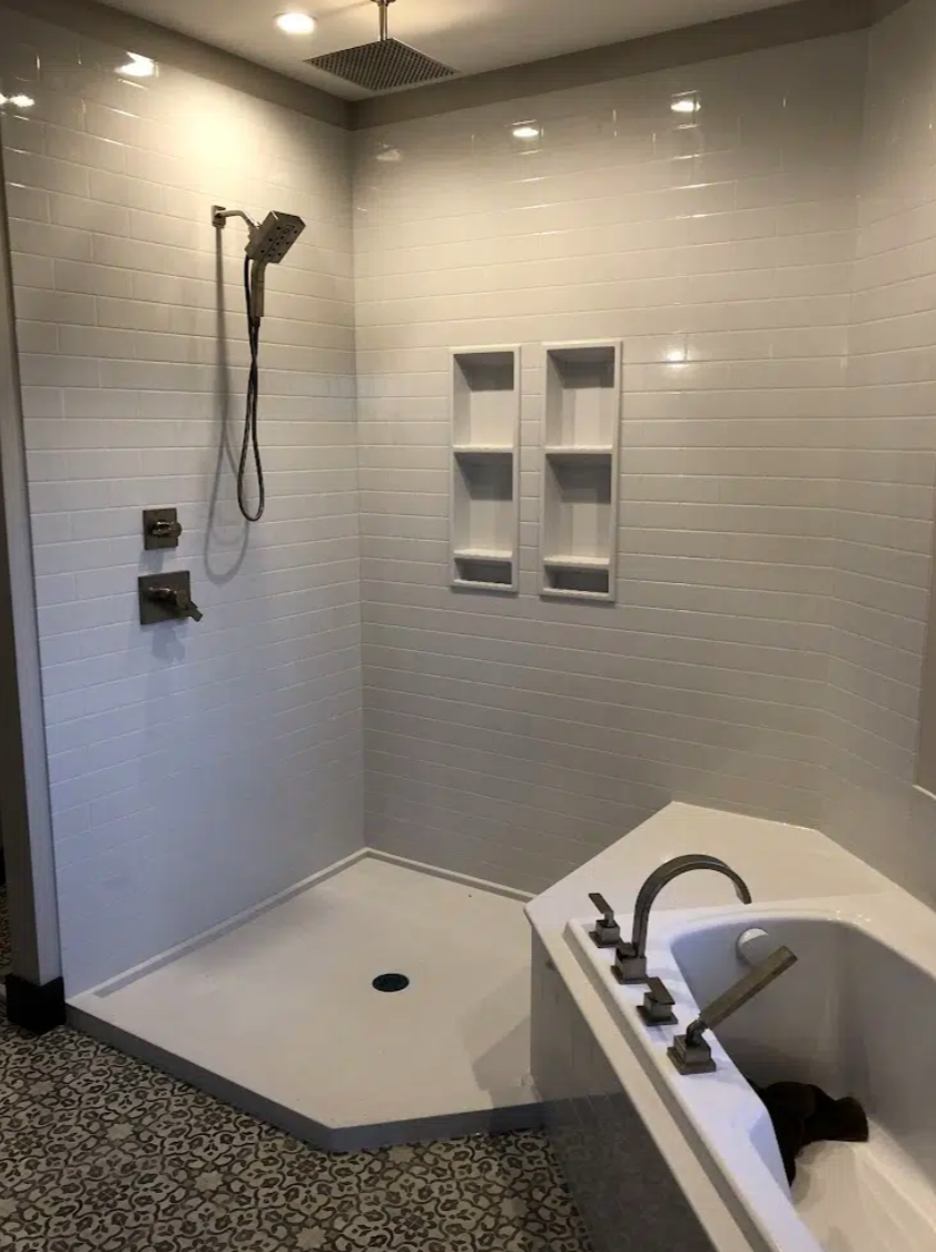 Newly renovated bathroom with a walk-in shower area, a built-in shelf, a rain shower head, and a bathtub with a faucet.