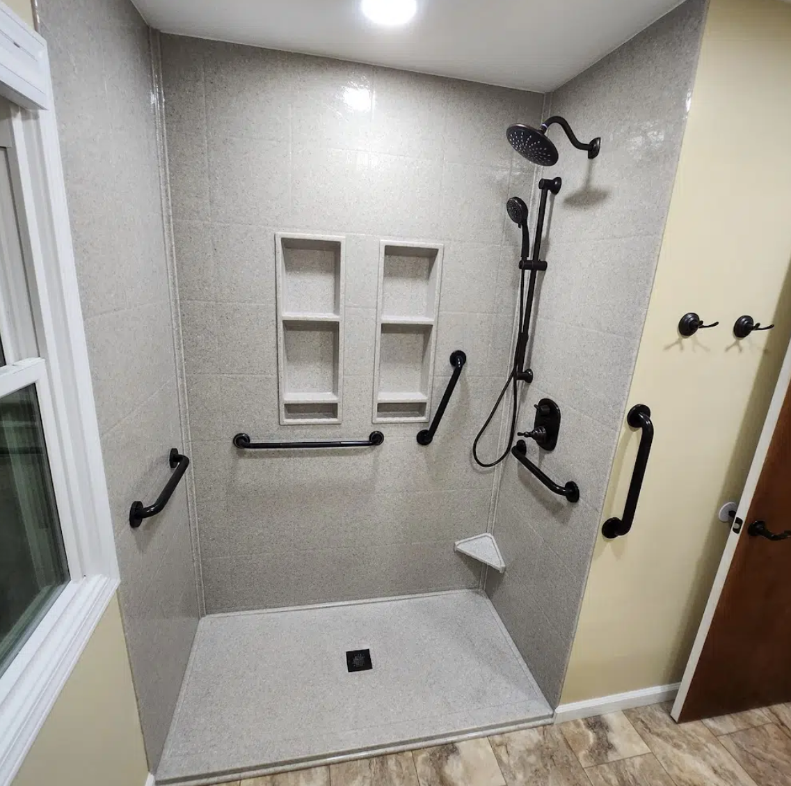 Accessible walk-in shower with multiple grab bars, a handheld showerhead, and built-in shelves.