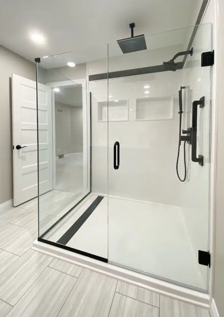 Clean modern walk-in shower with glass enclosure, black fixtures, and rain showerhead in a neutral-colored bathroom.