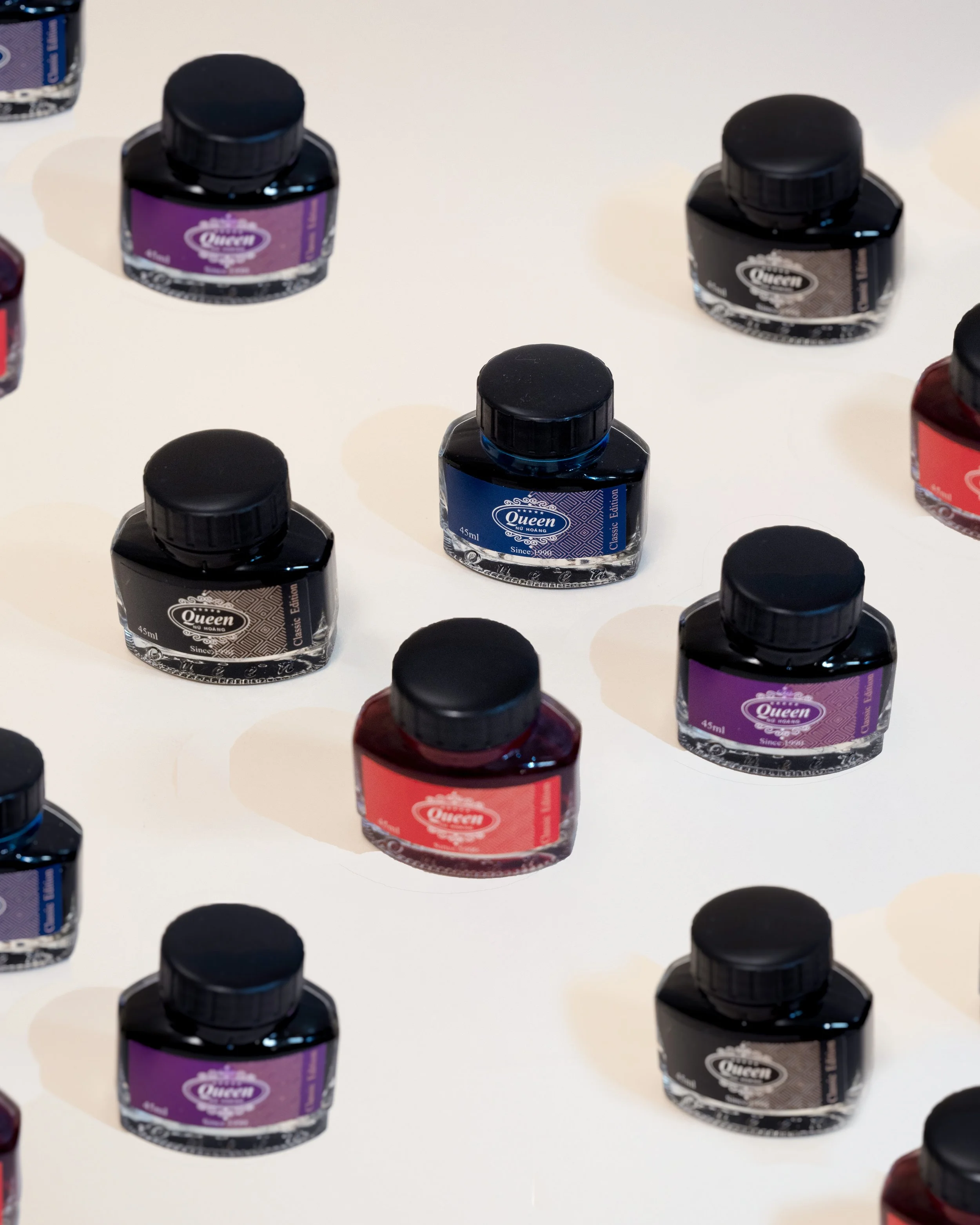 Multiple bottles of ink in various colors including black, purple, blue, and red, arranged on a white surface.