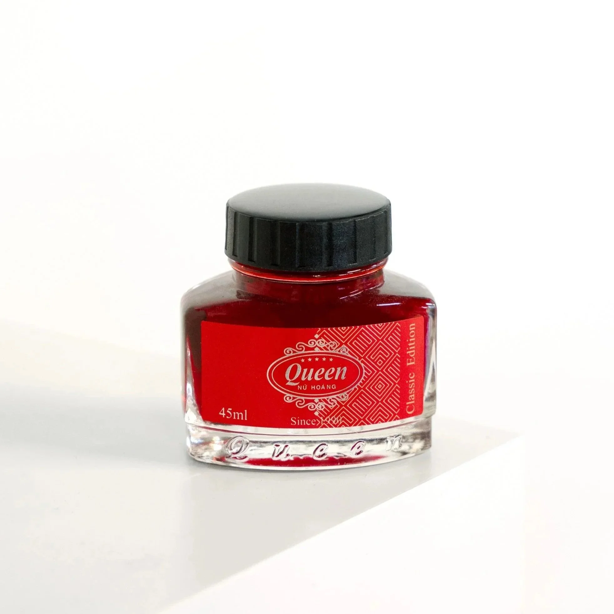 Red ink bottle labeled 'Queen Classic Edition' with a black cap on a white surface and background.