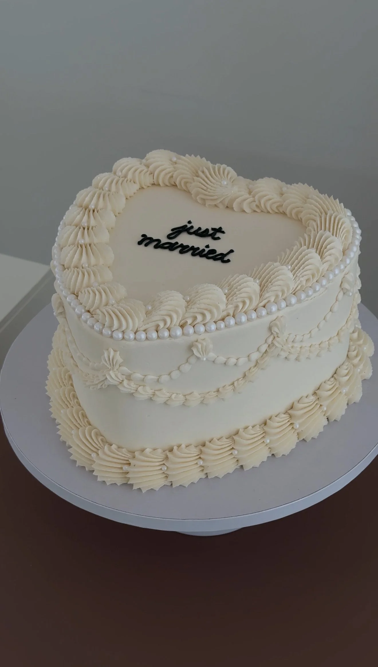 Two-tiered wedding cake with cream piping, pearl decorations, and the words "just married" written on top.