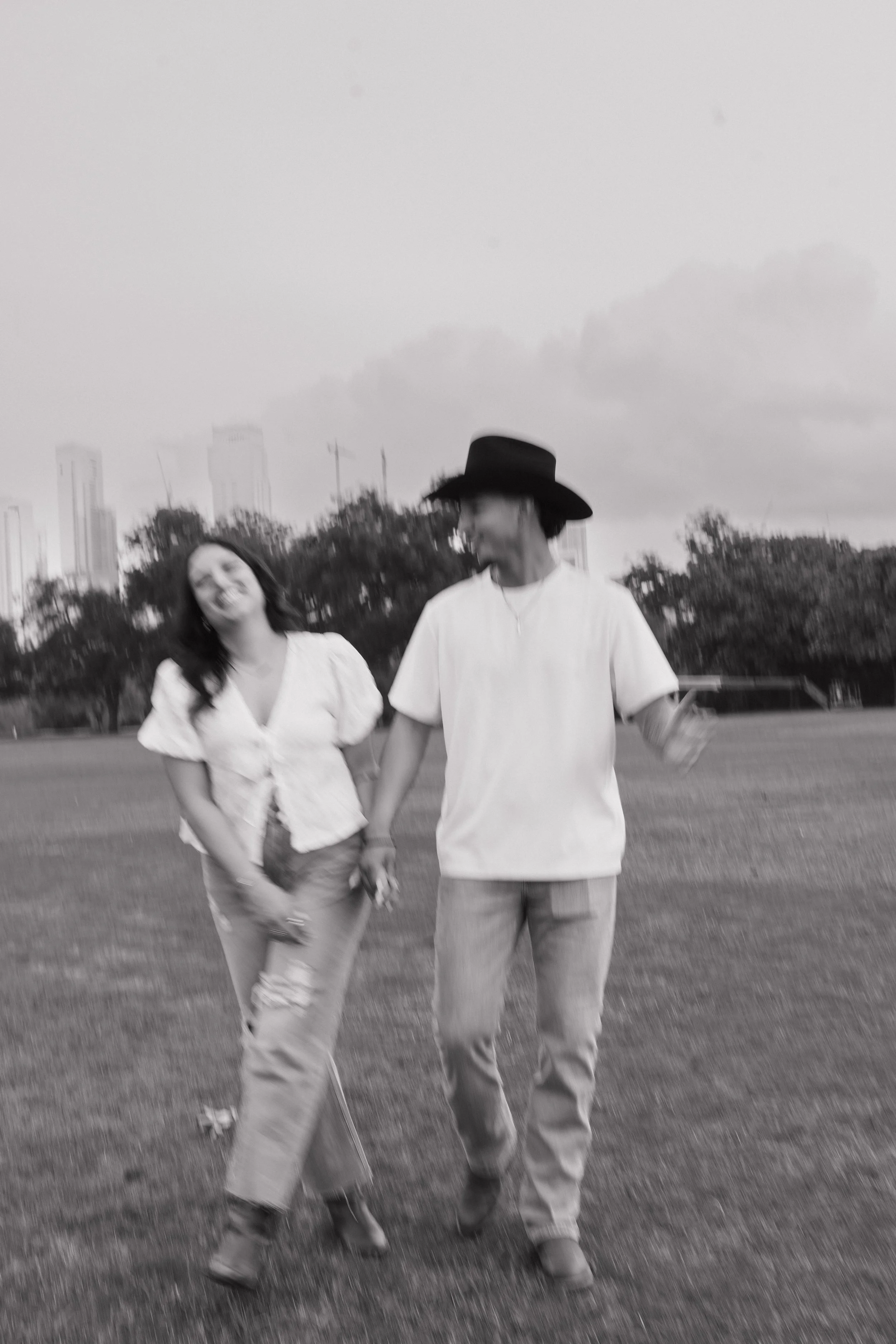 A couple walking hand-in-hand on a grassy field, smiling and enjoying each other's company, in black and white.