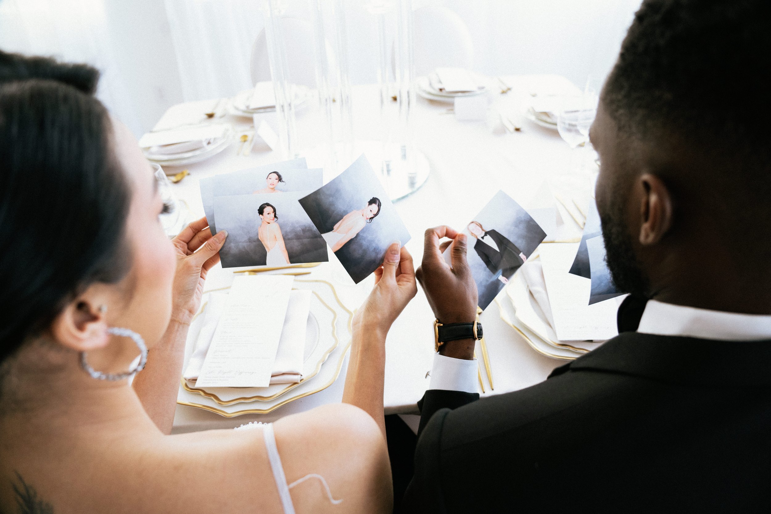 A man and a woman sit at a table, looking at photographs of models, possibly for a wedding or fashion event.