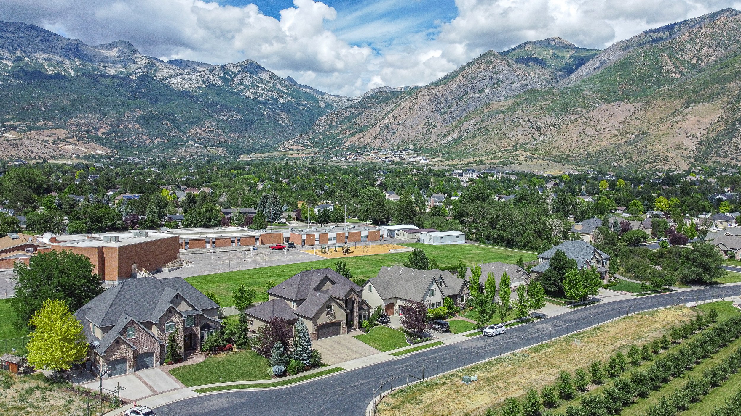 Aerial view of a suburban neighborhood next to a large body of water, with mountains in the background and a clear blue sky.