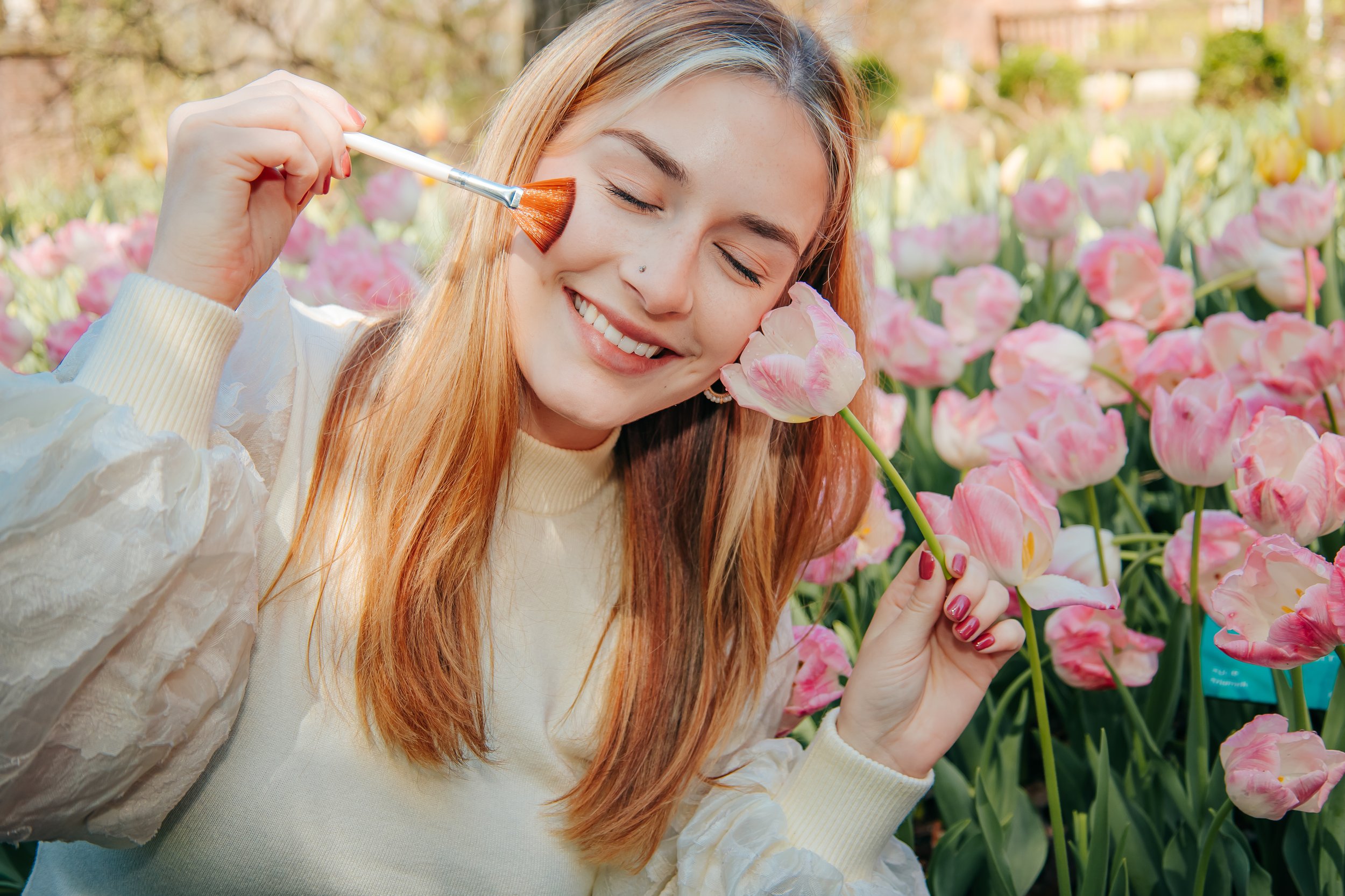 A young woman with long reddish hair smiling while holding a pink tulip in a field of pink tulips, enjoying a sunny day. Dixon gallery. Business branding Memphis photographer.