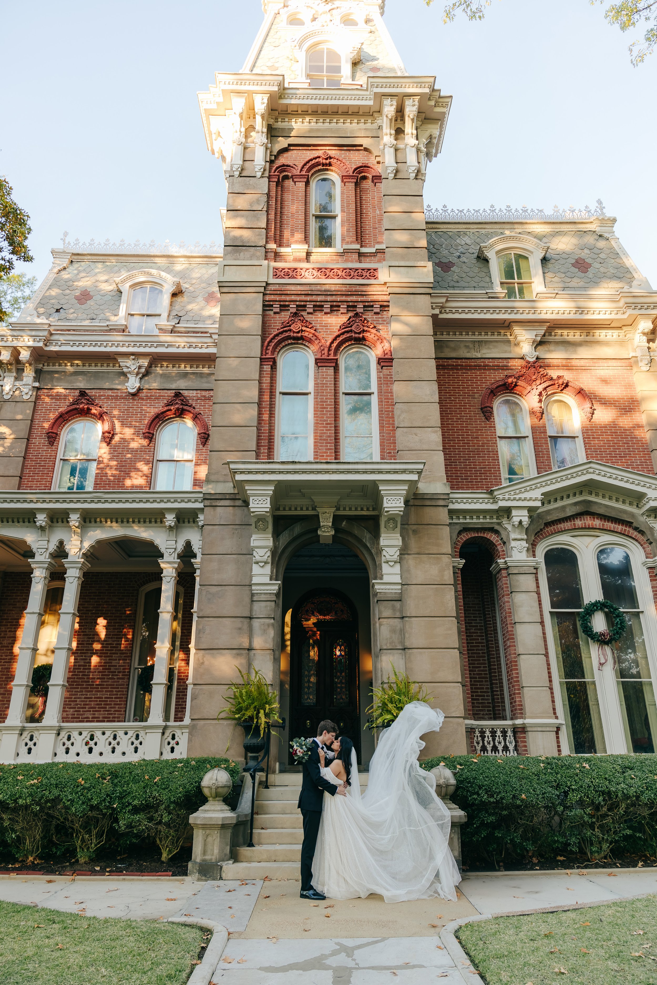A bride and groom stand in front of a large, historic brick house with ornate architecture. Woodruff Fontaine Museum. Memphis wedding photographer