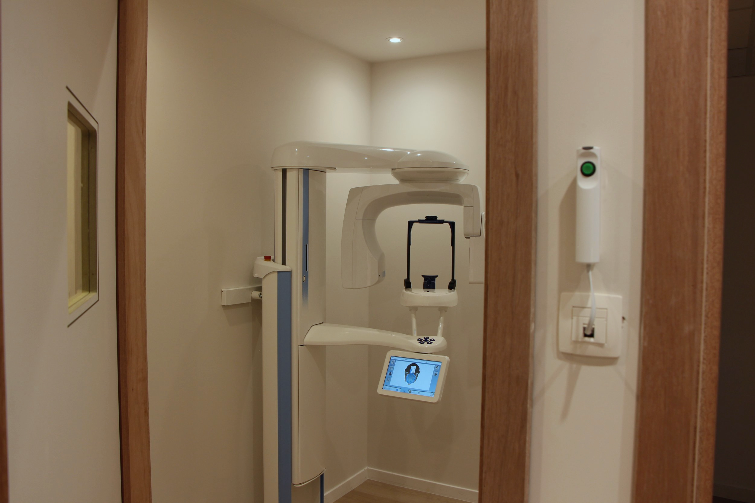 Appareil de radiologie dentaire dans une salle de clinique, vue partielle depuis l'entrée.