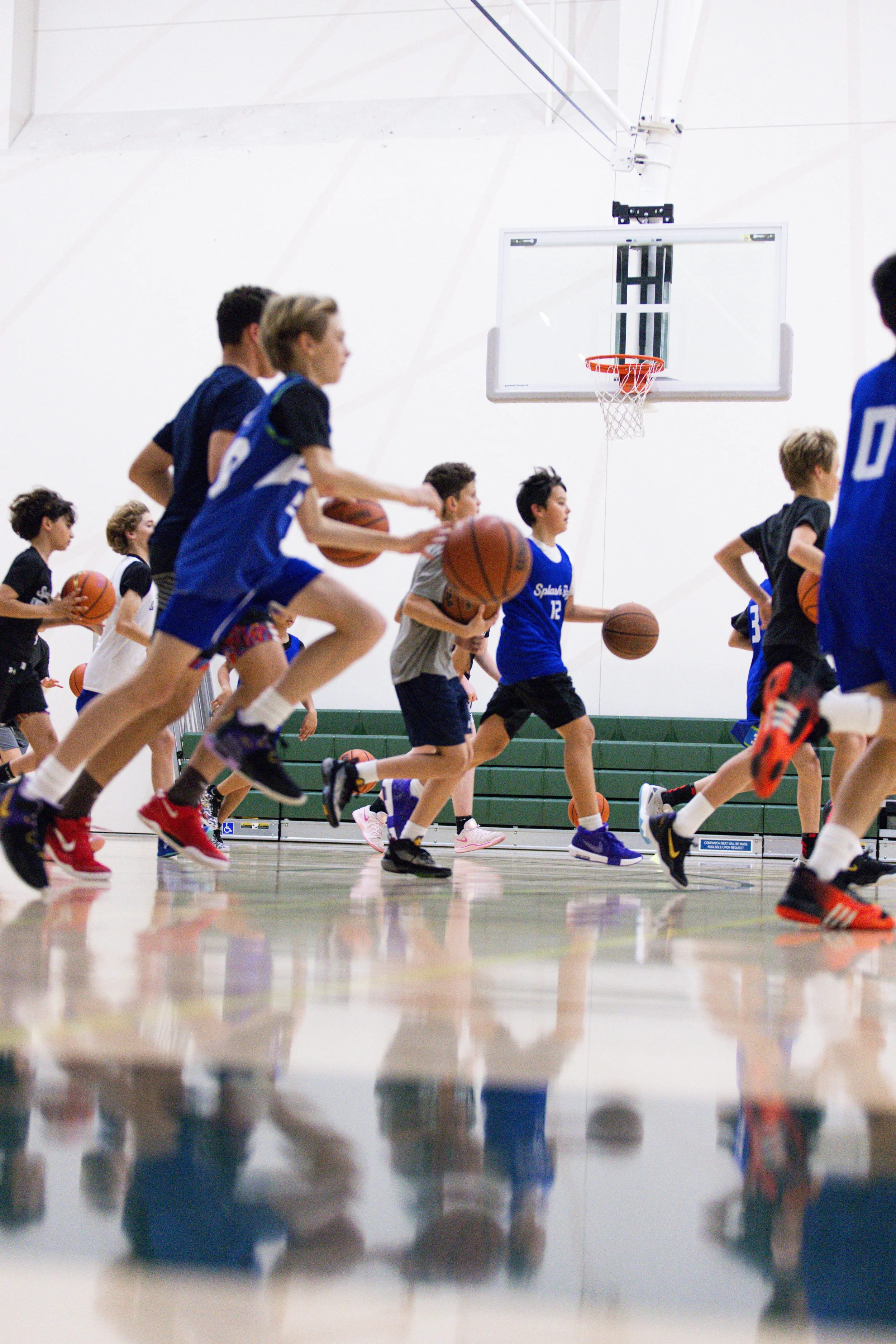 Group of children running on a basketball court, holding basketballs, during practice or drill session.