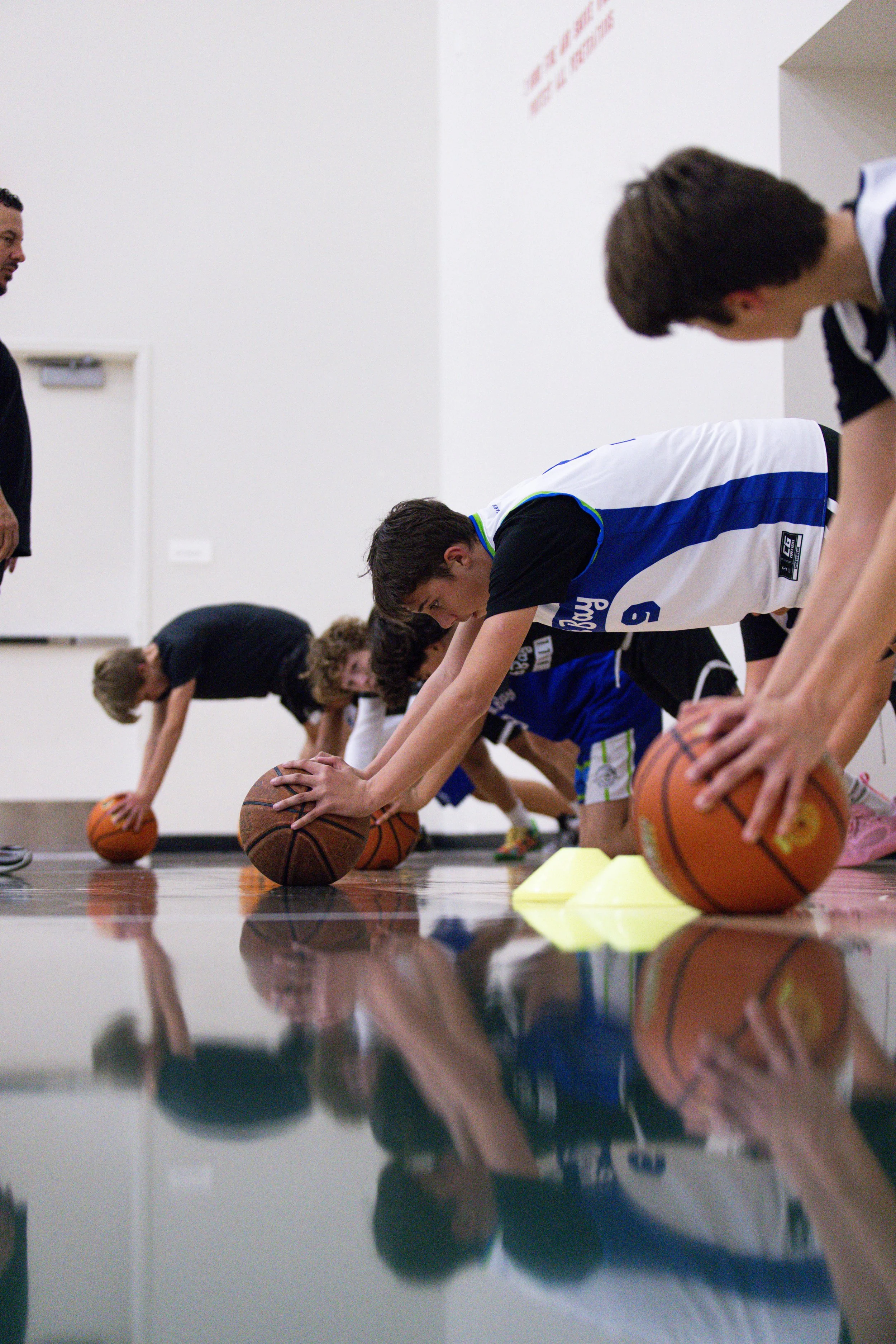 Young basketball players practicing on the court with a coach supervising.