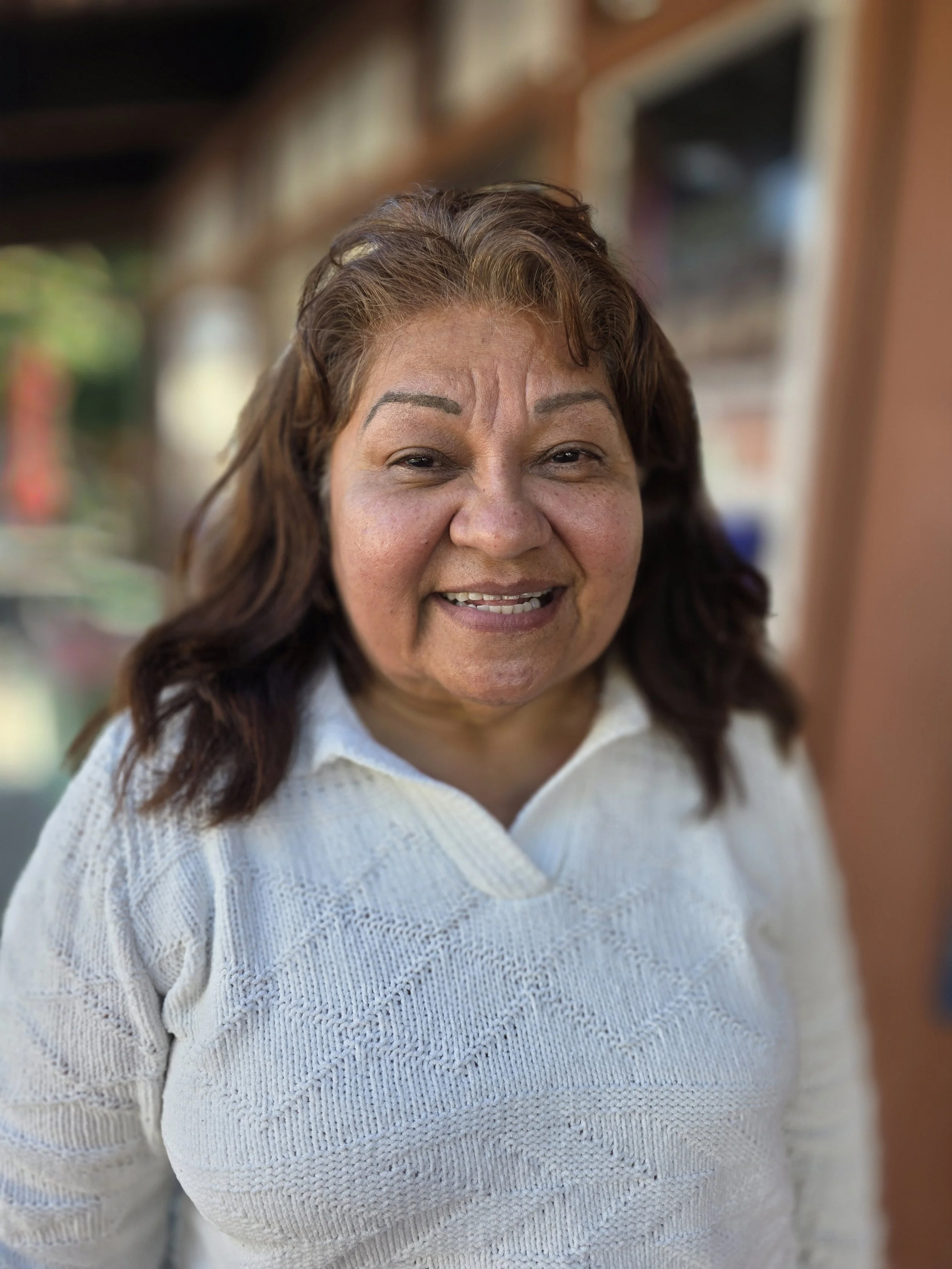 A smiling woman with wavy brown hair wearing a white collared sweater.