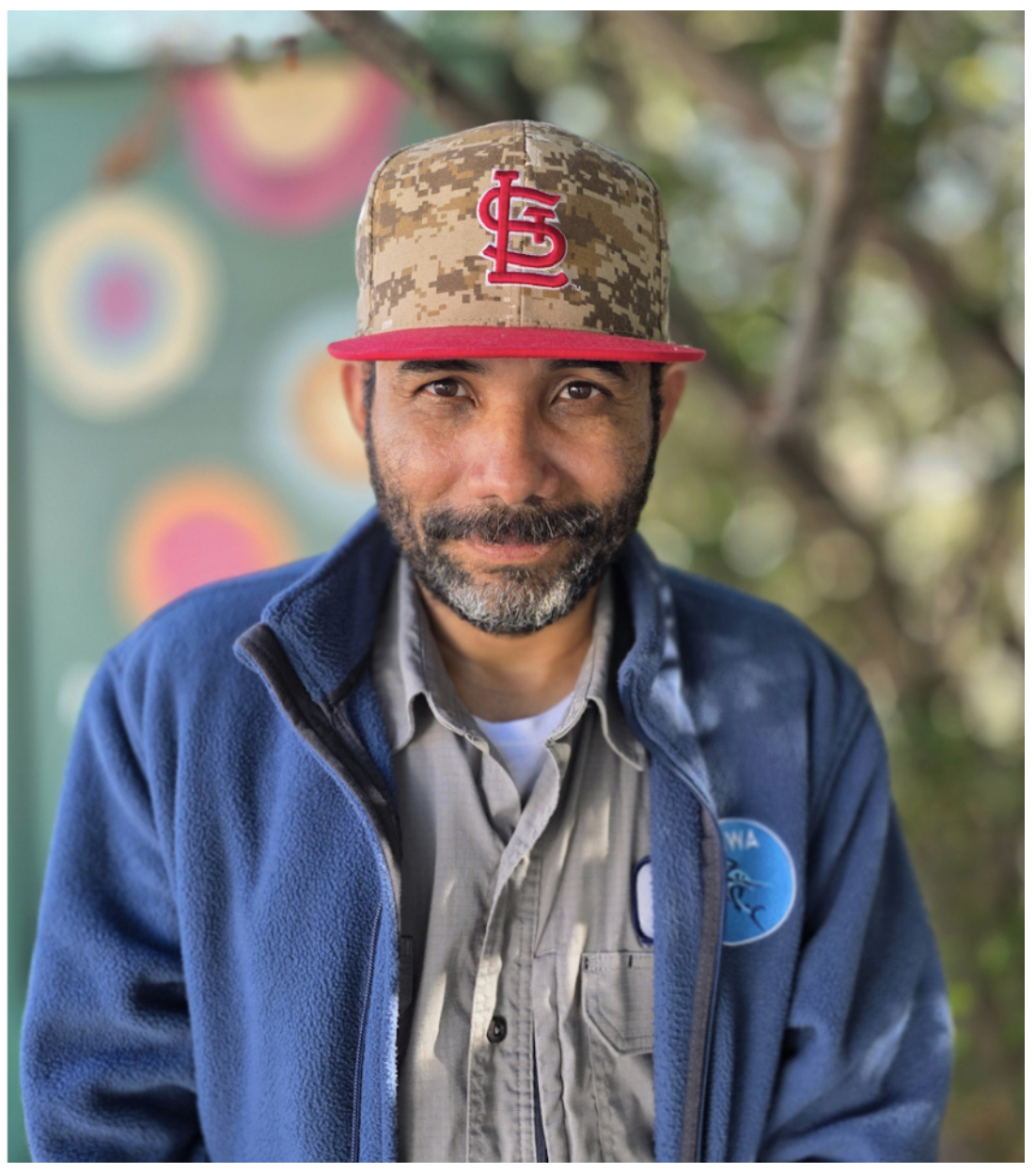 A man wearing a St Louis hat and a blue zip jacket, with a salt and pepper beard and mustache.