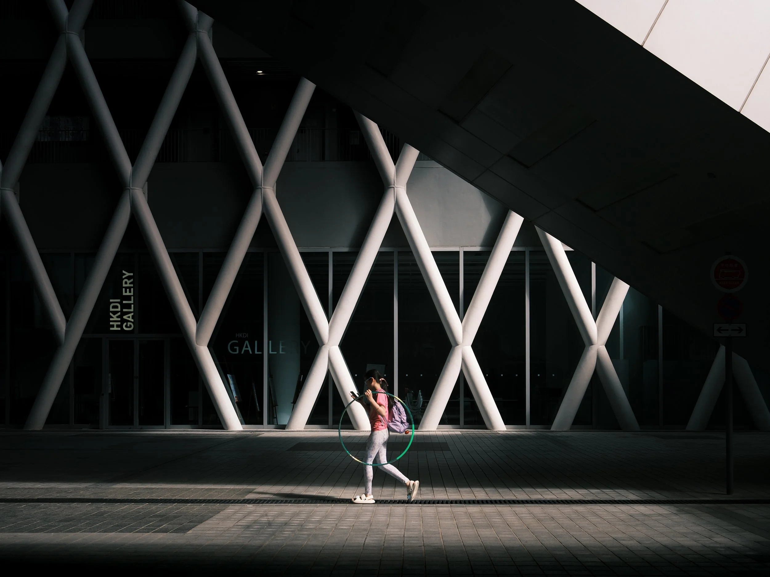 The Hoop Girl: A teenager walks through the Hong Kong Design Institute, basked in midday sunlight, capturing a serene moment of daily life.