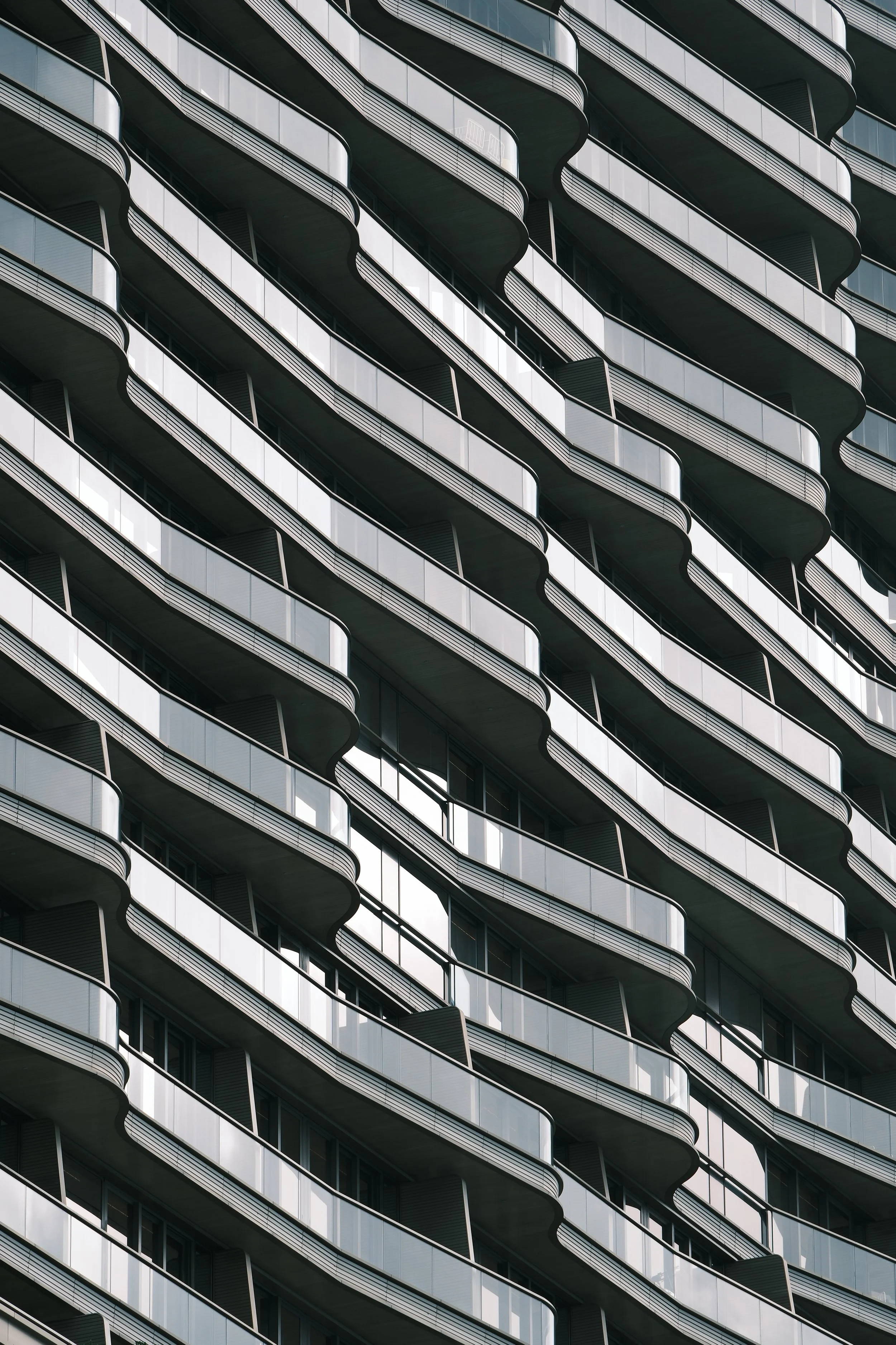 Close-up view of a modern high-rise building with repeating pattern of glass balconies and dark metal railings.