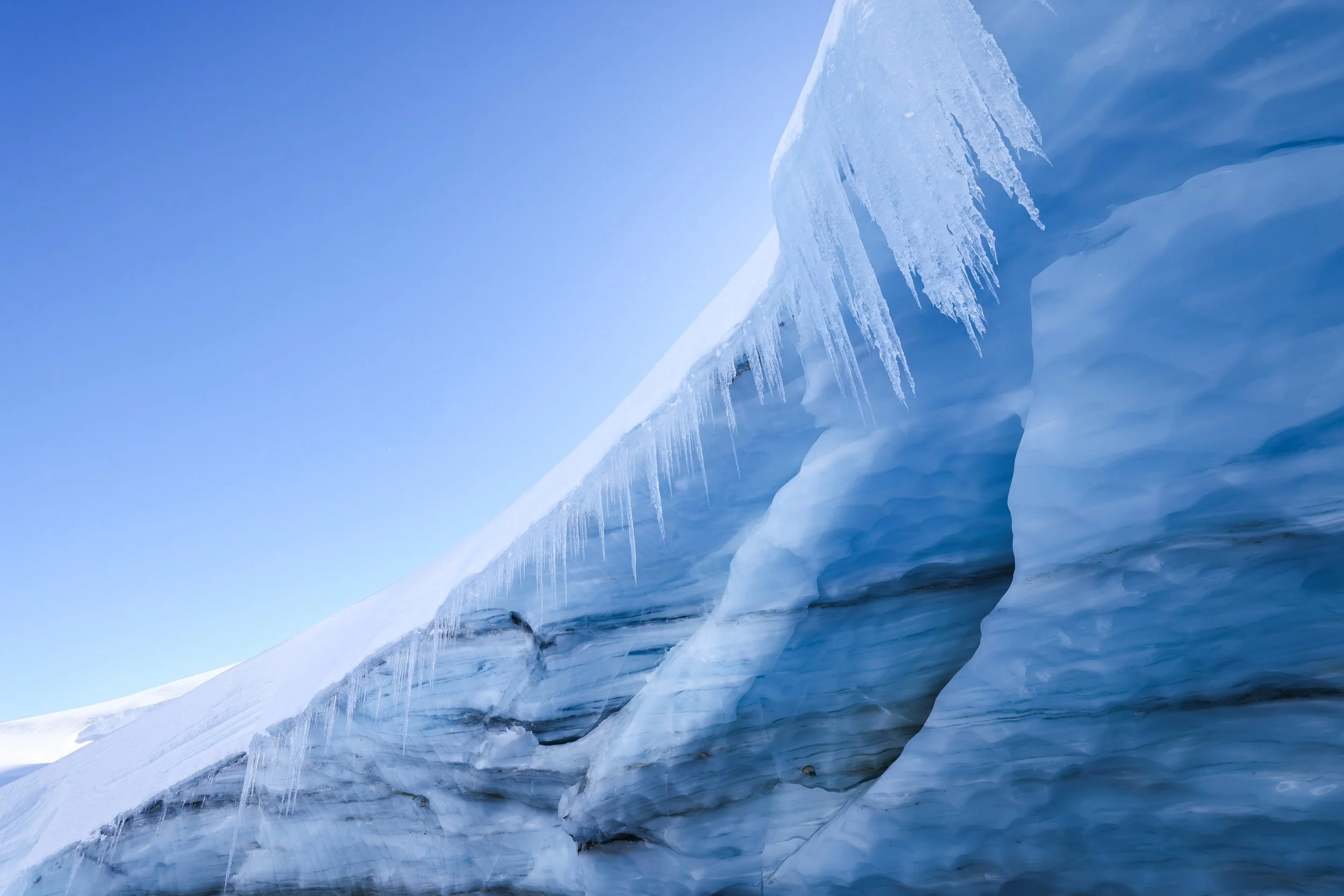 Close-up of a glacier with icicles hanging from the edge against a clear blue sky.