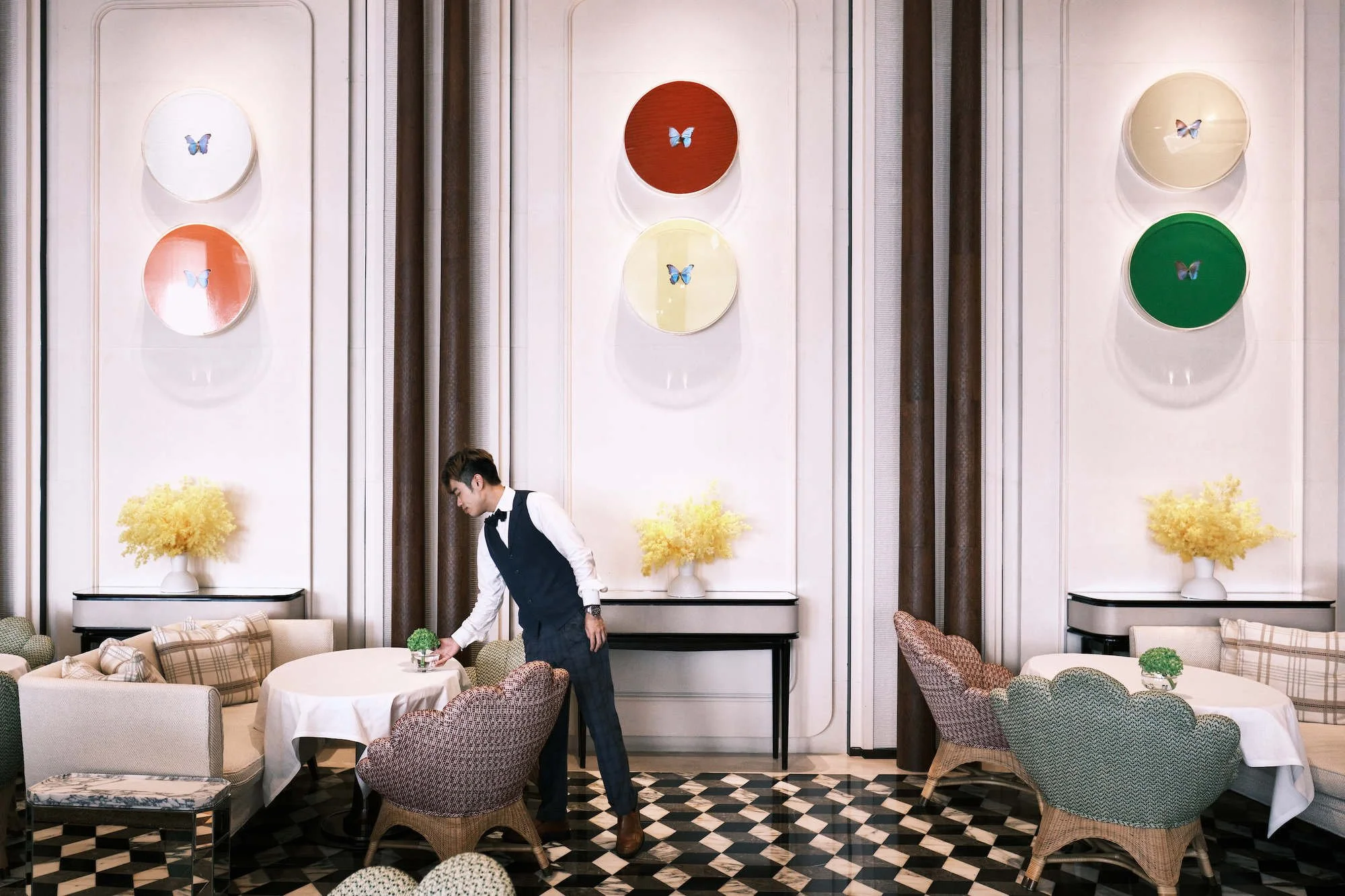 A young man dressed in a suit and bow tie setting a table at in a dining room at the Rosewood Hotel in Hong Kong.