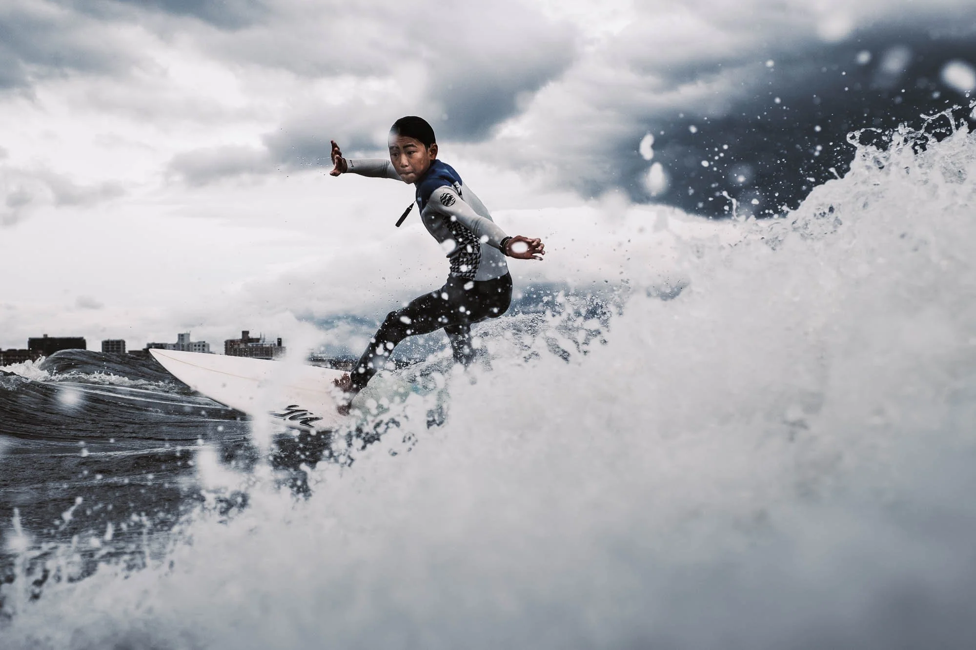 Close-up shot of a young Japanese surfer riding a wave with spray hitting the camera lens.