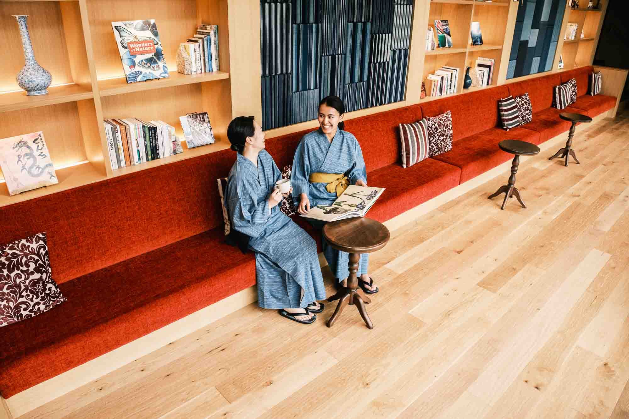 Two women wearing traditional yukata clothing sit and converse in the hotel’s lounge.
