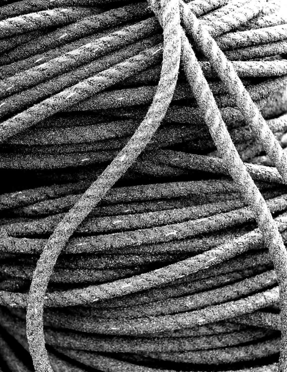  Close-up of a coiled rope covered in grains of sand, a textured black and white detail from “The Shore” series by Japan travel photographer Ben Weller. 