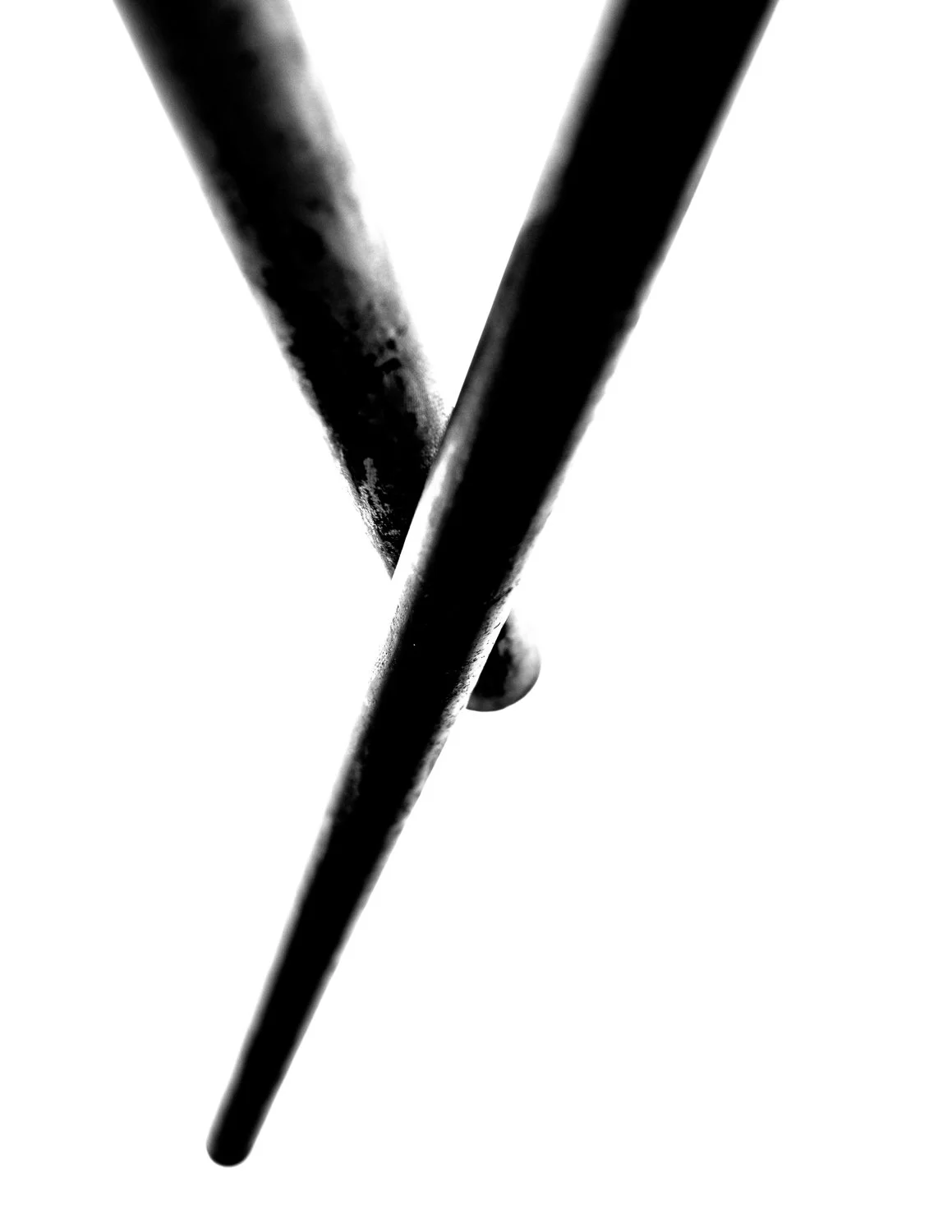   Abstract black and white photograph of two weathered poles crossing diagonally, part of “The Shore” series exploring coastal life in Kanagawa Prefecture.  