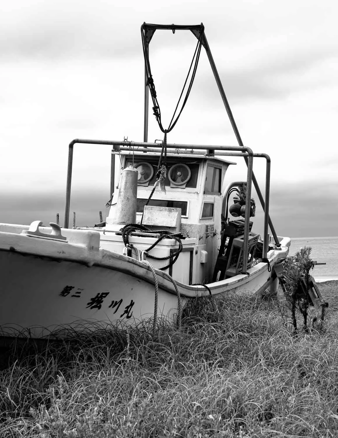  Fishing boat resting in the grass on the shore in Kanagawa Prefecture, captured as part of a black and white travel photography project by Japan photographer Ben Weller. 