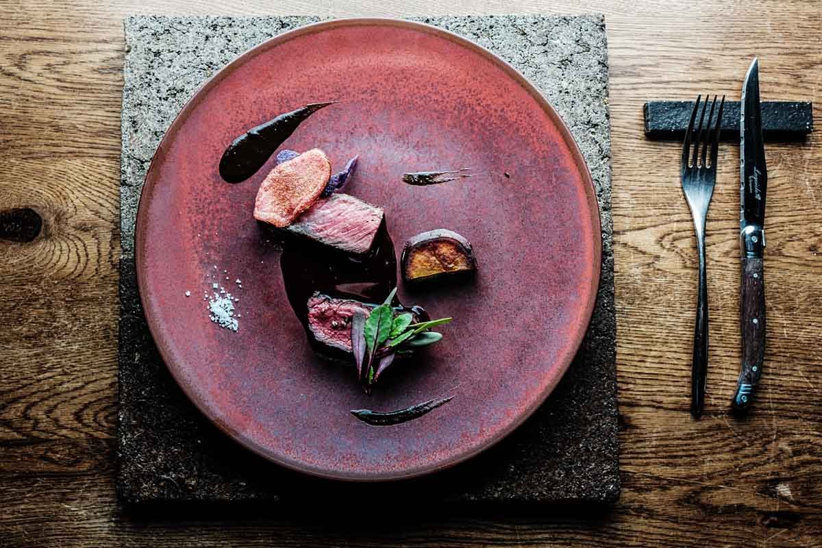  Oyama-san grills thick cuts of beef and venison on the wood fire. He pairs the meat with fermented black garlic and red wine venison sauces, and serves it alongside sautéed sweet potato. 