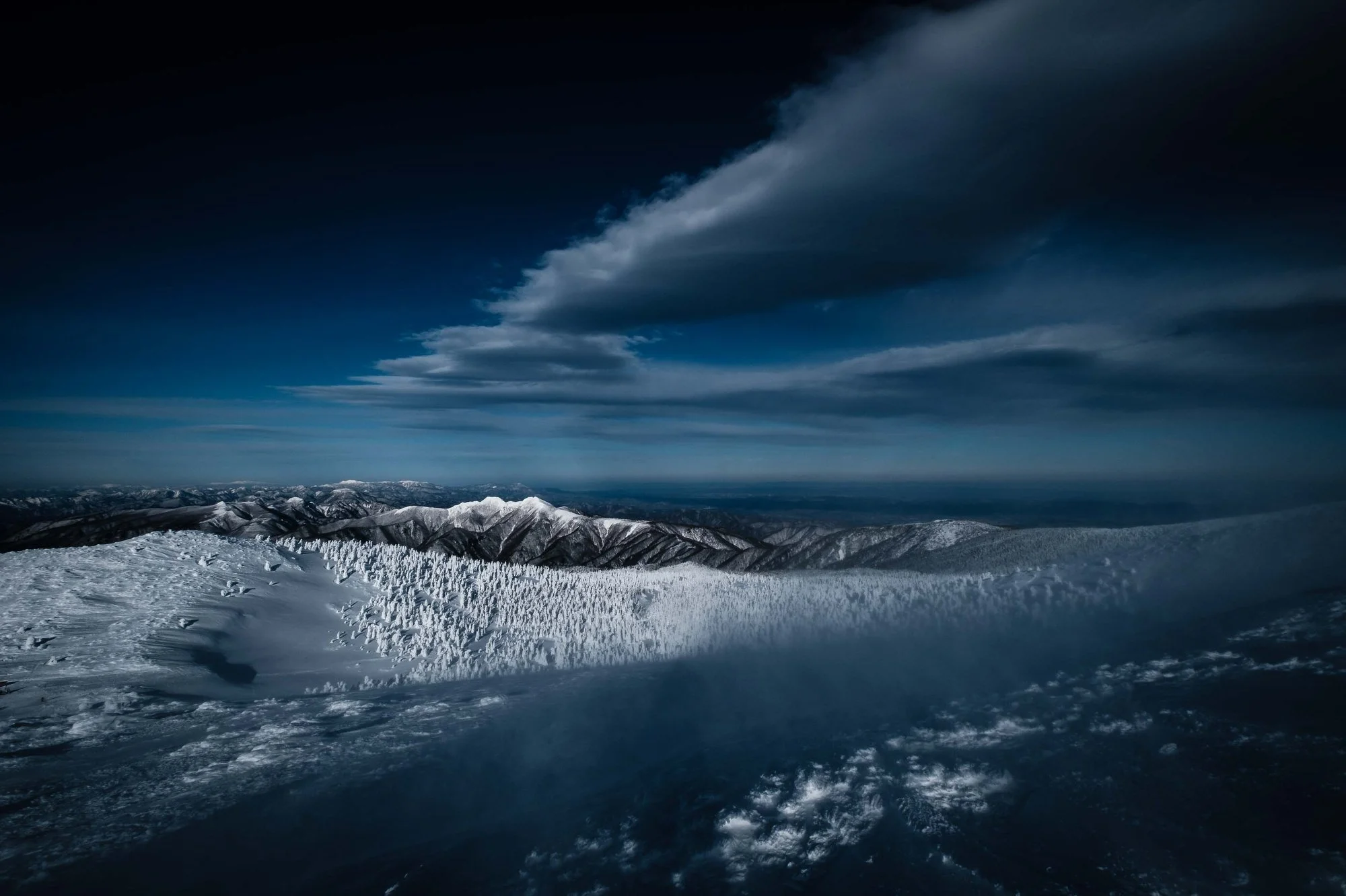Snow-covered mountain range under a cloudy sky in Tohoku.