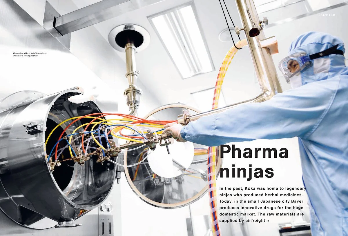 Scientist in protective gear working with laboratory machinery to produce drugs, with colorful pipes and equipment in a clean, sterile lab environment.