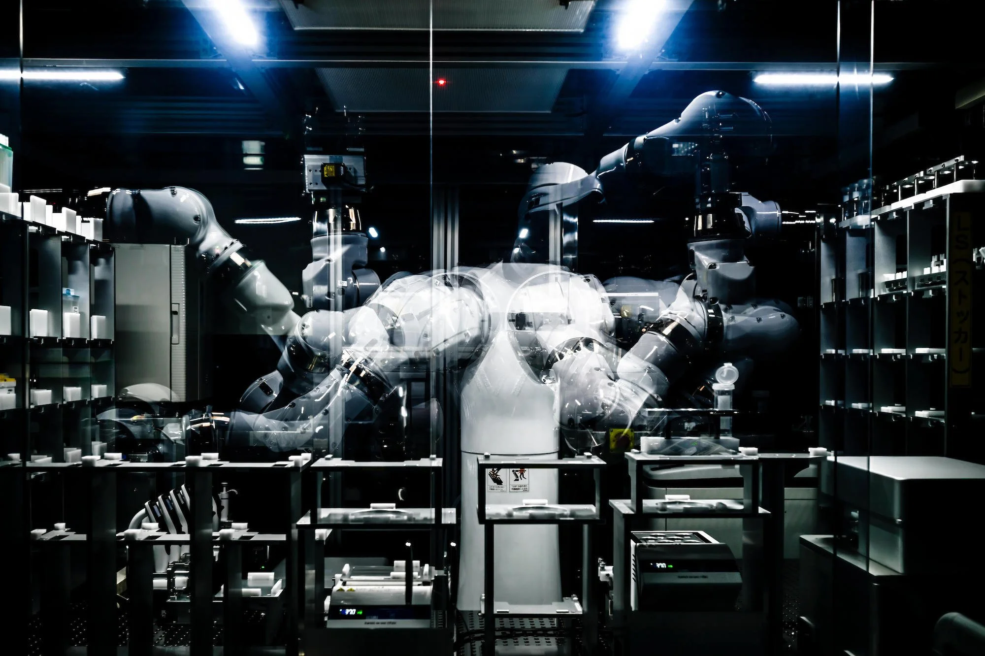 Industrial robotic arms inside a glass enclosure in a high-tech laboratory.