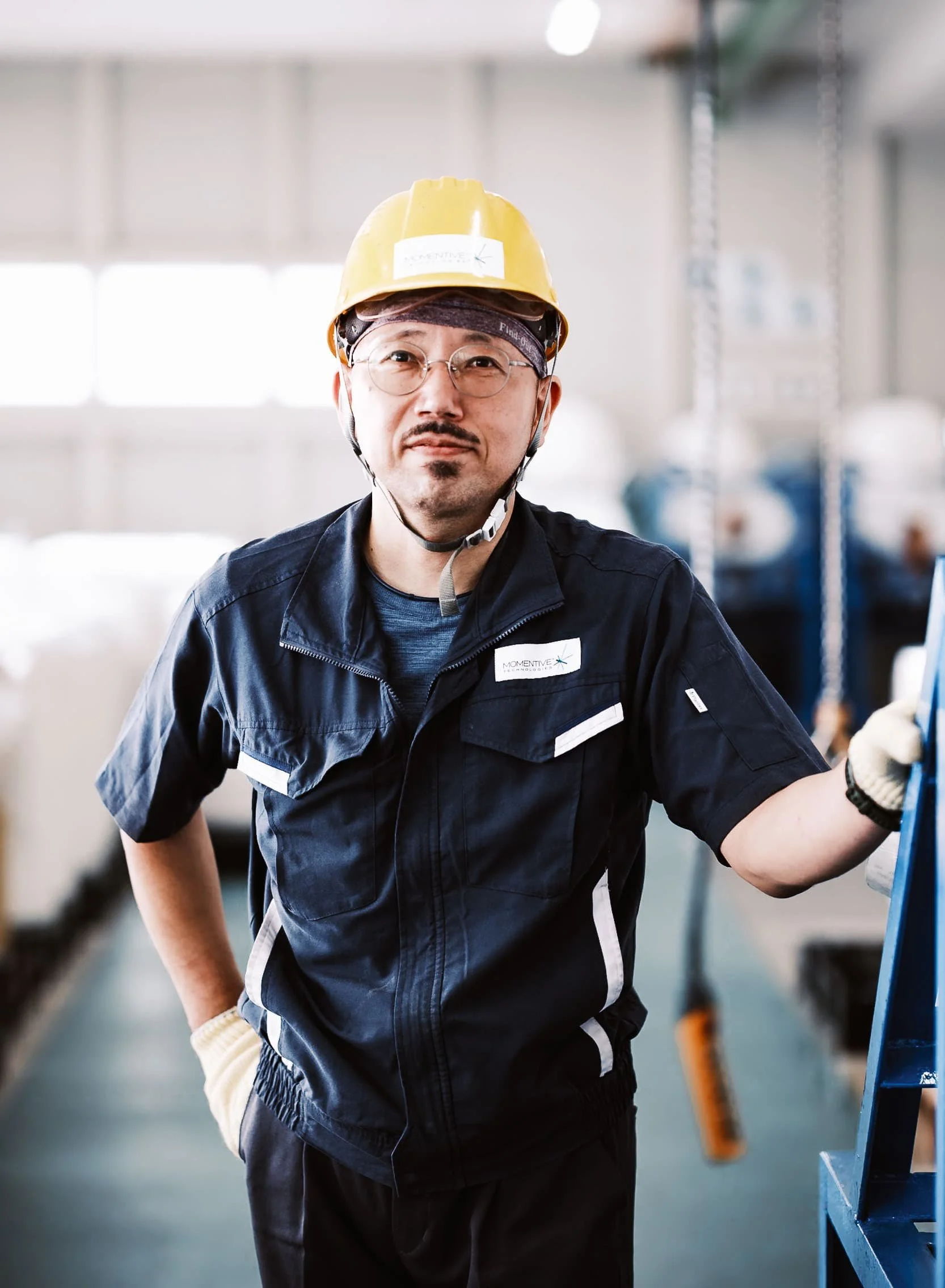 A worker wearing a hardhat poses for a portrait in an industrial warehouse.