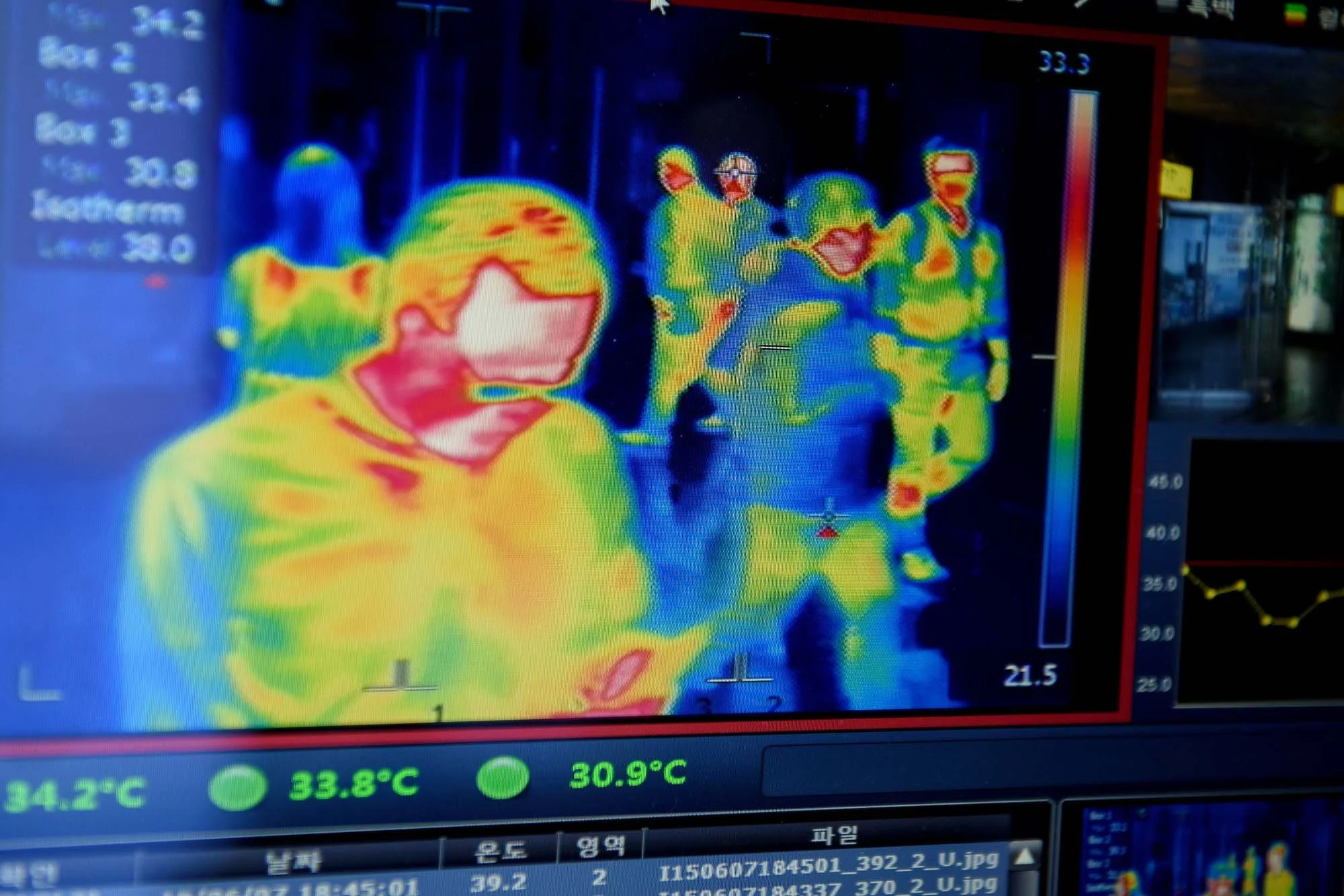 Thermal image of a group of people walking indoors, showing temperature variations with colors from blue to red. The person in front has the hottest temperature, with others behind them.