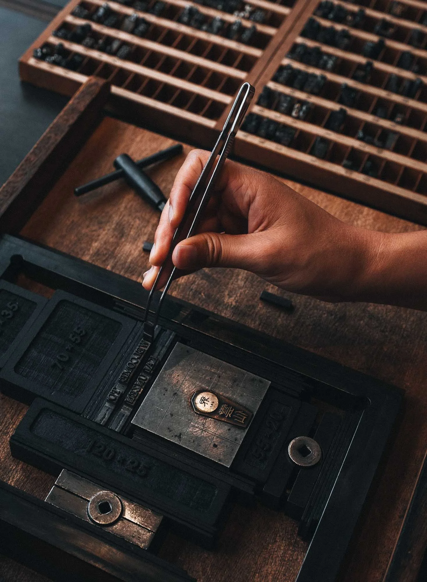 A person uses tweezers to handle metal type on a letterpress at Kai Unzen resort.