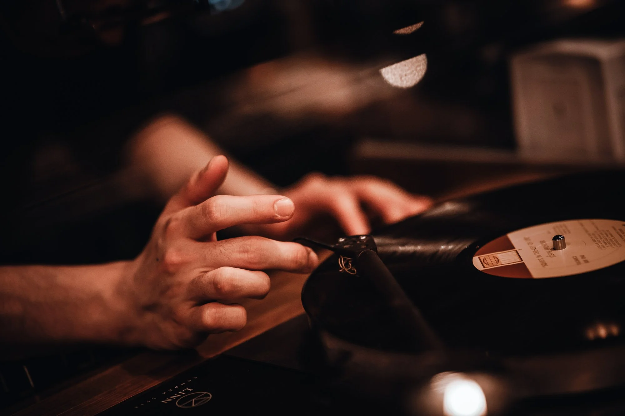 A person’s hand handling a vinyl record on a turntable in a dimly lit setting.