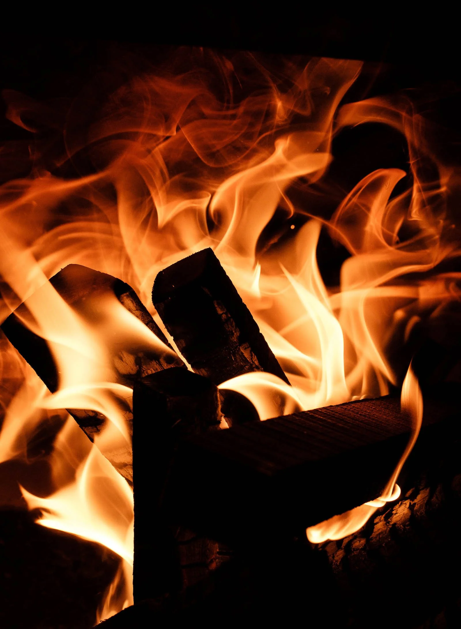 Close-up of burning wood logs in a fire with orange flames and dark background.