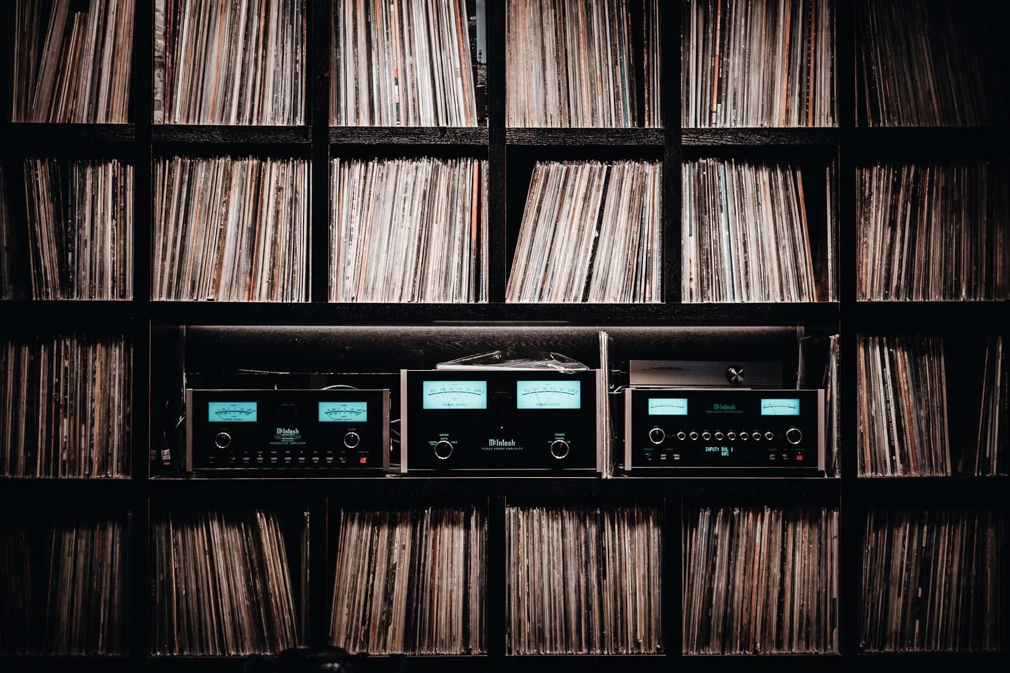 A vast vinyl record collection organized on wall shelves with vintage audio equipment in a Tokyo listening bar.
